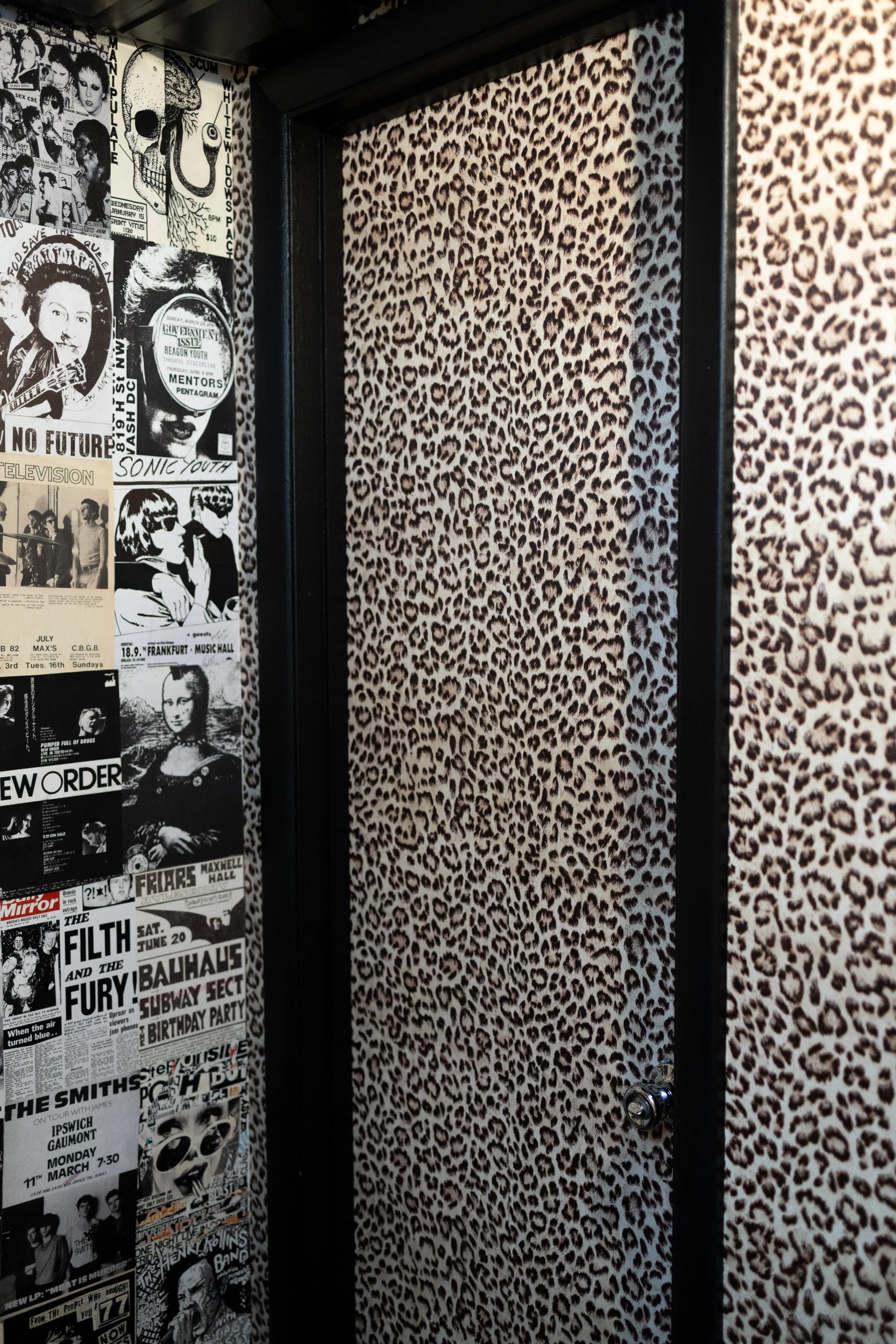 Door with animal print wallpaper and a wall covered with black and white posters and flyers for music and events.