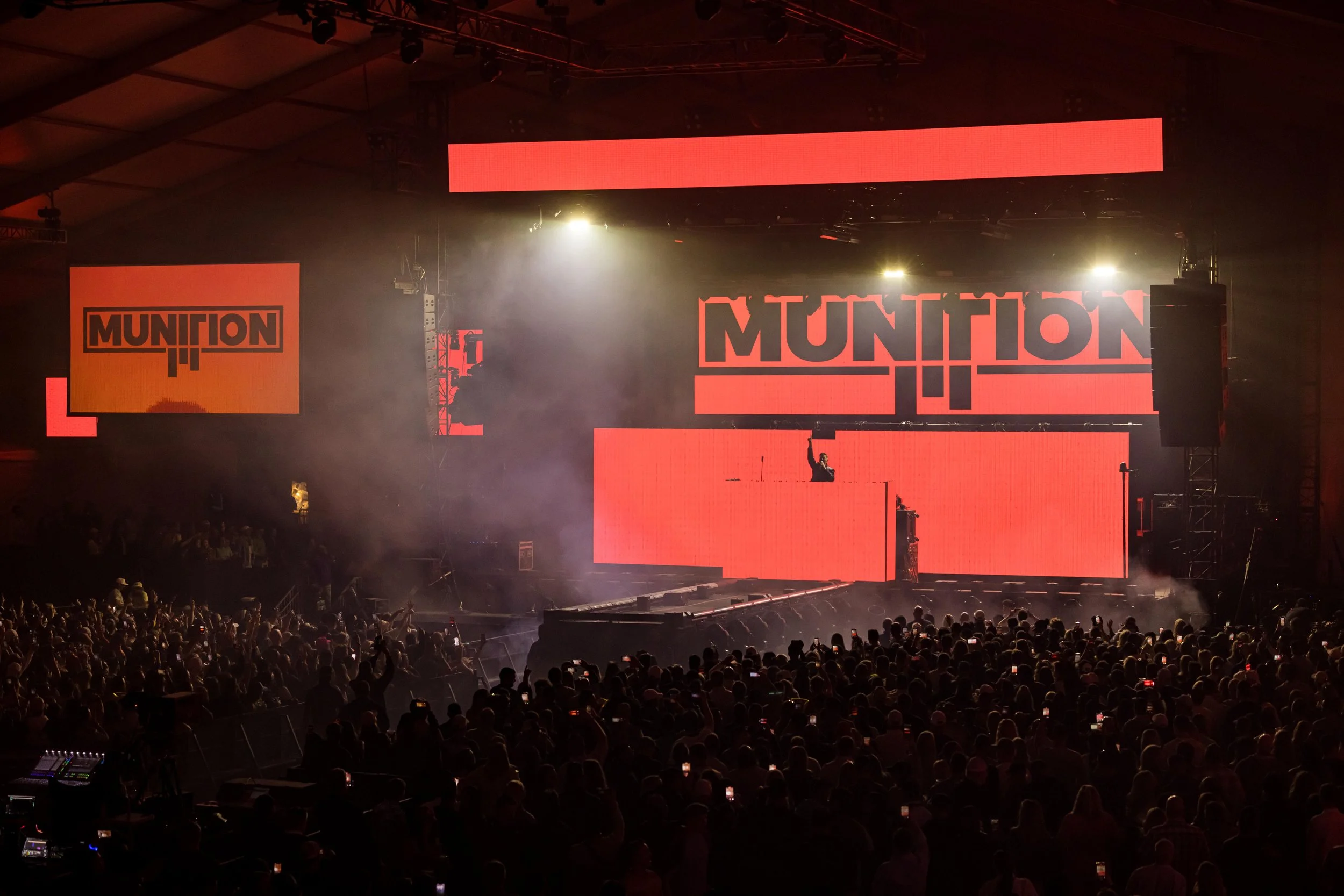 The Birds Nest at the WM Phoenix Open scene with large crowd, illuminated stage featuring orange screens displaying the word 'MUNITION', and a performer raising their hand.