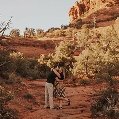 A couple embracing in a scenic desert landscape with red rock formations and sparse vegetation.