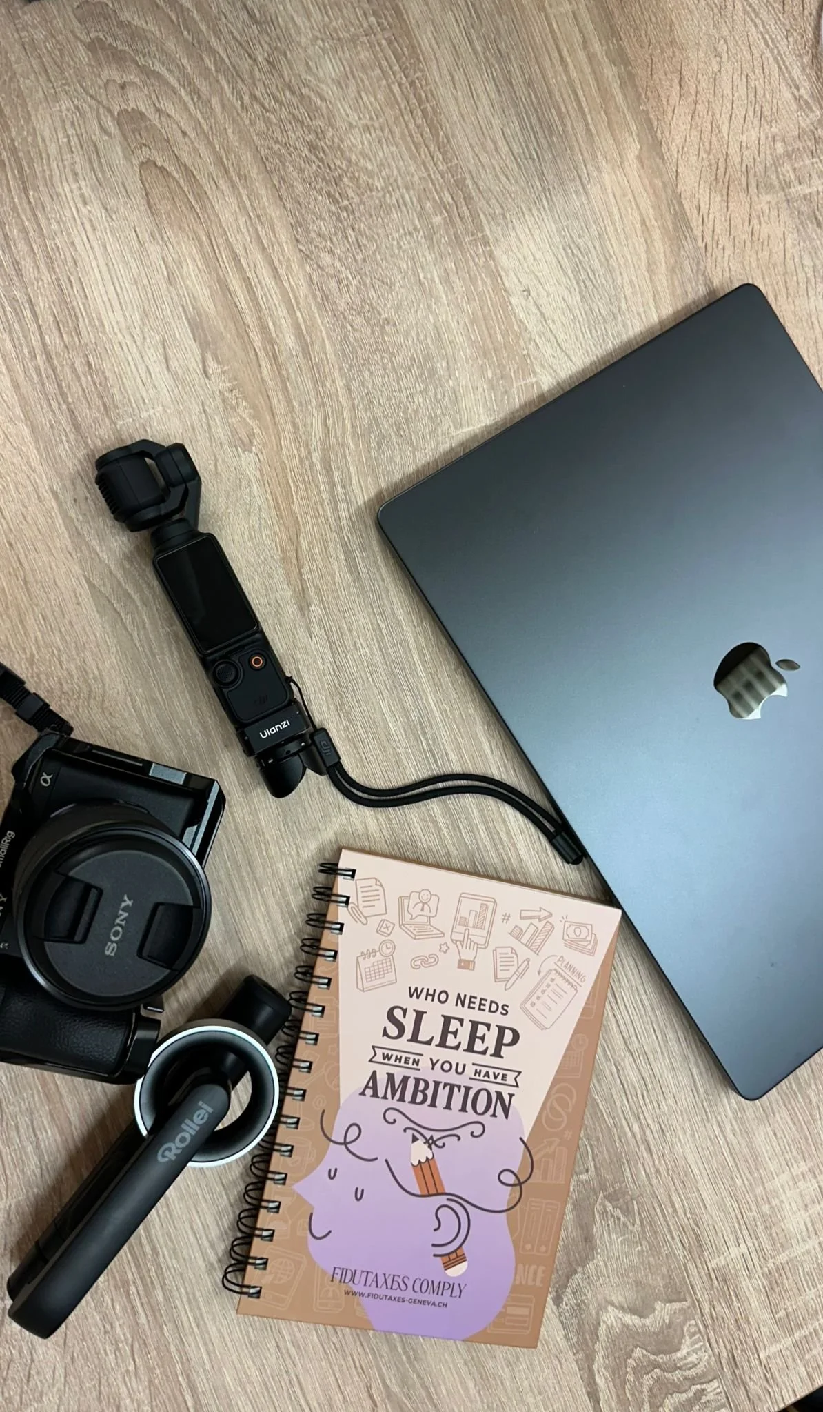 Un ordinateur portable, une caméra Sony, osmo pocket 3, un carnet avec une citation sur le sommeil et l'ambition. La vie d'entrepreneur