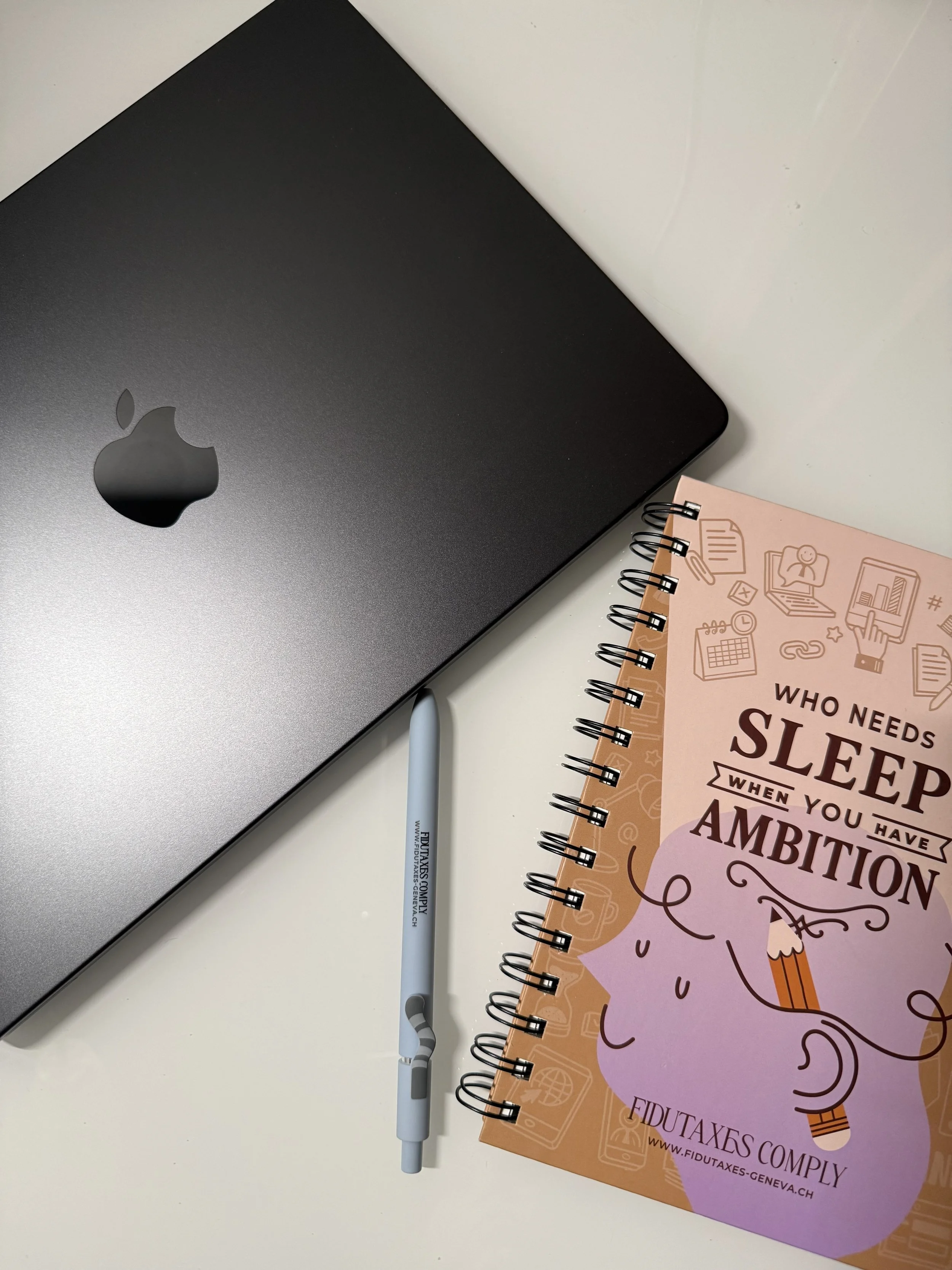 Un ordinateur portable noir, un stylo et un carnet avec des illustrations et le texte "Who needs sleep when you have ambition".