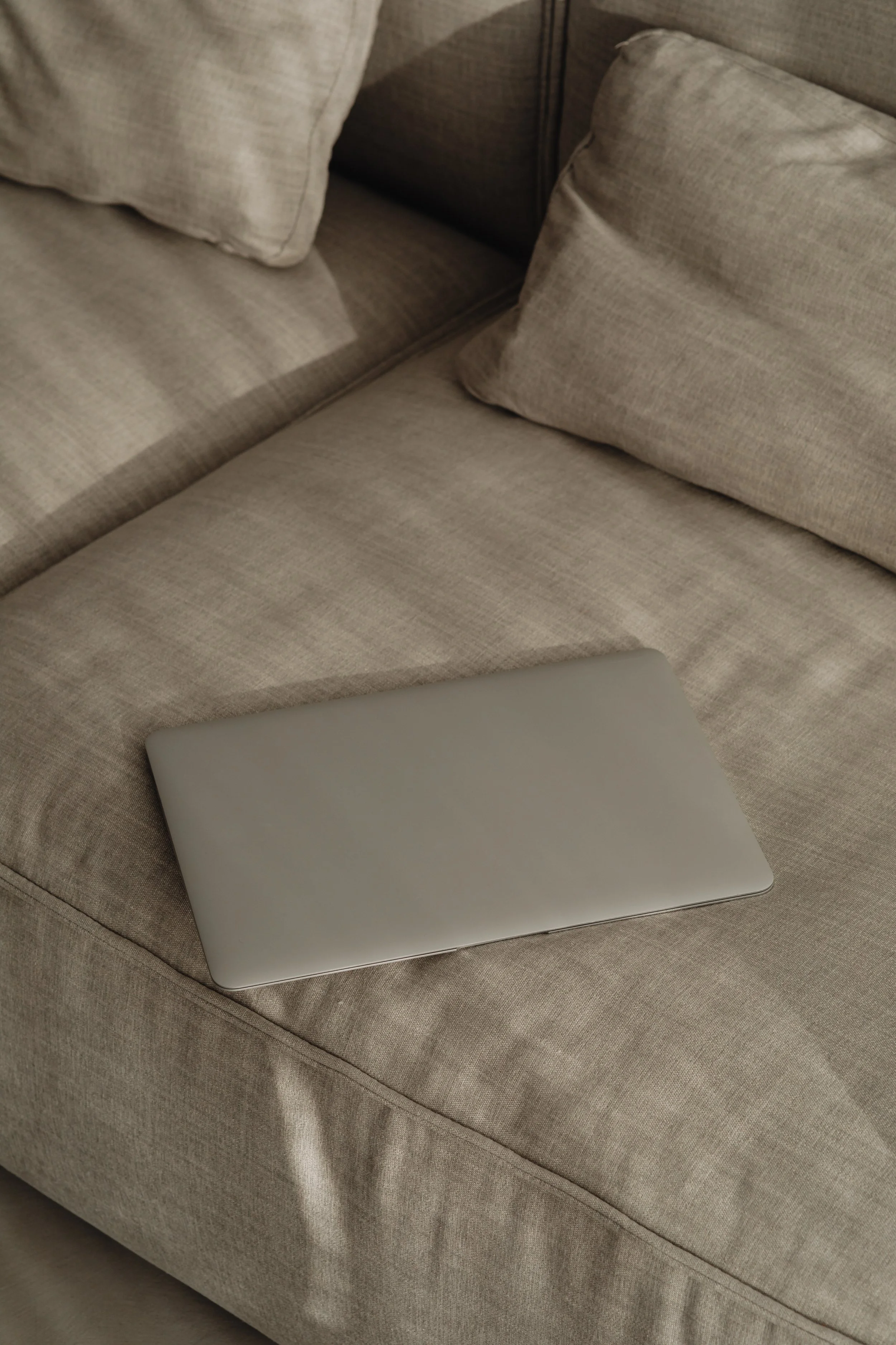 Laptop argenté posé sur un canapé beige avec des coussins.