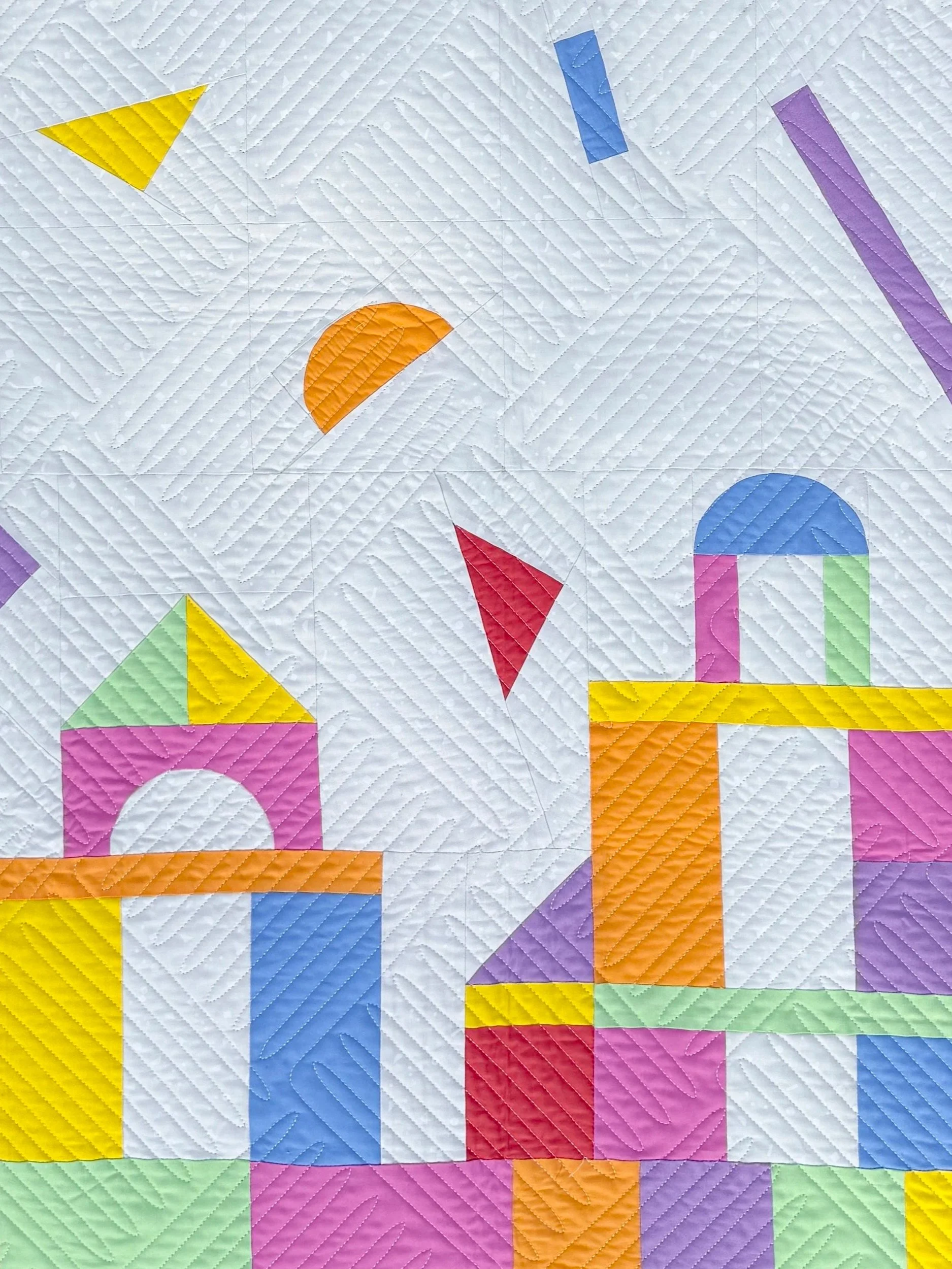 Colorful quilt with geometric patterns including triangles, circles, and rectangles in various bright colors like yellow, red, blue, purple, orange, and green on a white background.