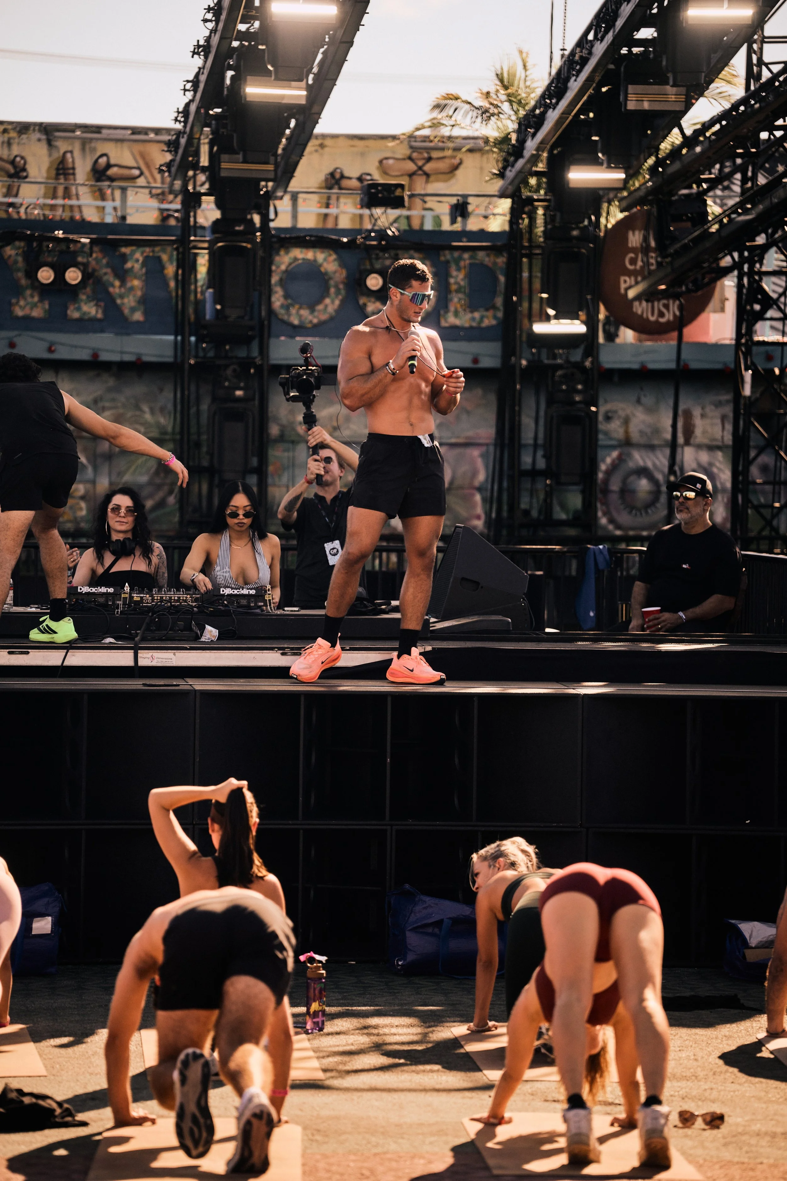 Instructor leading a high-energy fitness and movement class on an outdoor stage, blending music, wellness, and community-driven lifestyle culture.