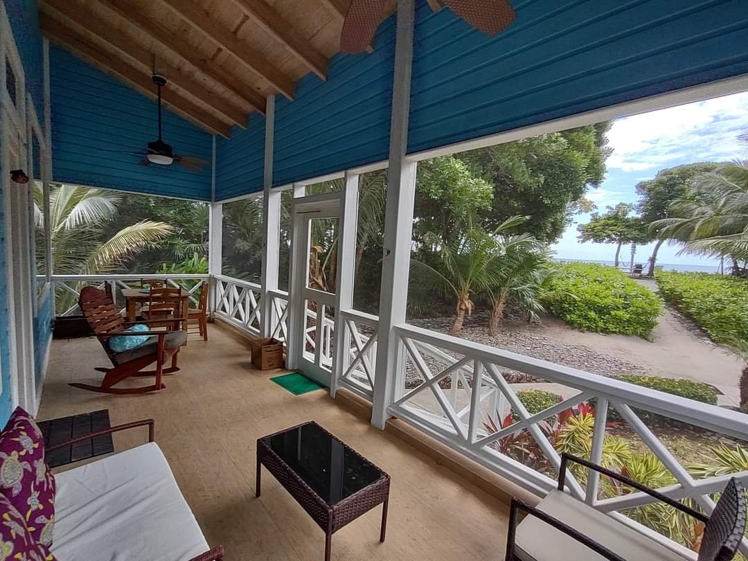 Covered porch with seating overlooking tropical greenery and a beach path.
