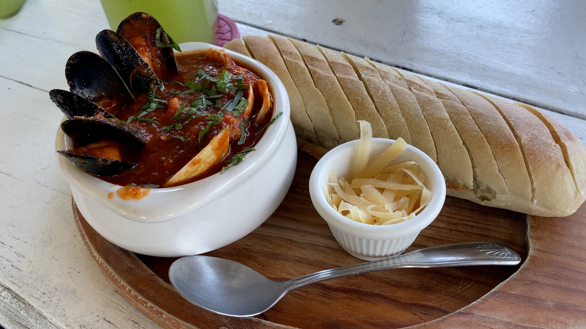 Seafood stew with mussels, in a white bowls, served with sliced bread and shredded cheese on a wooden platter.