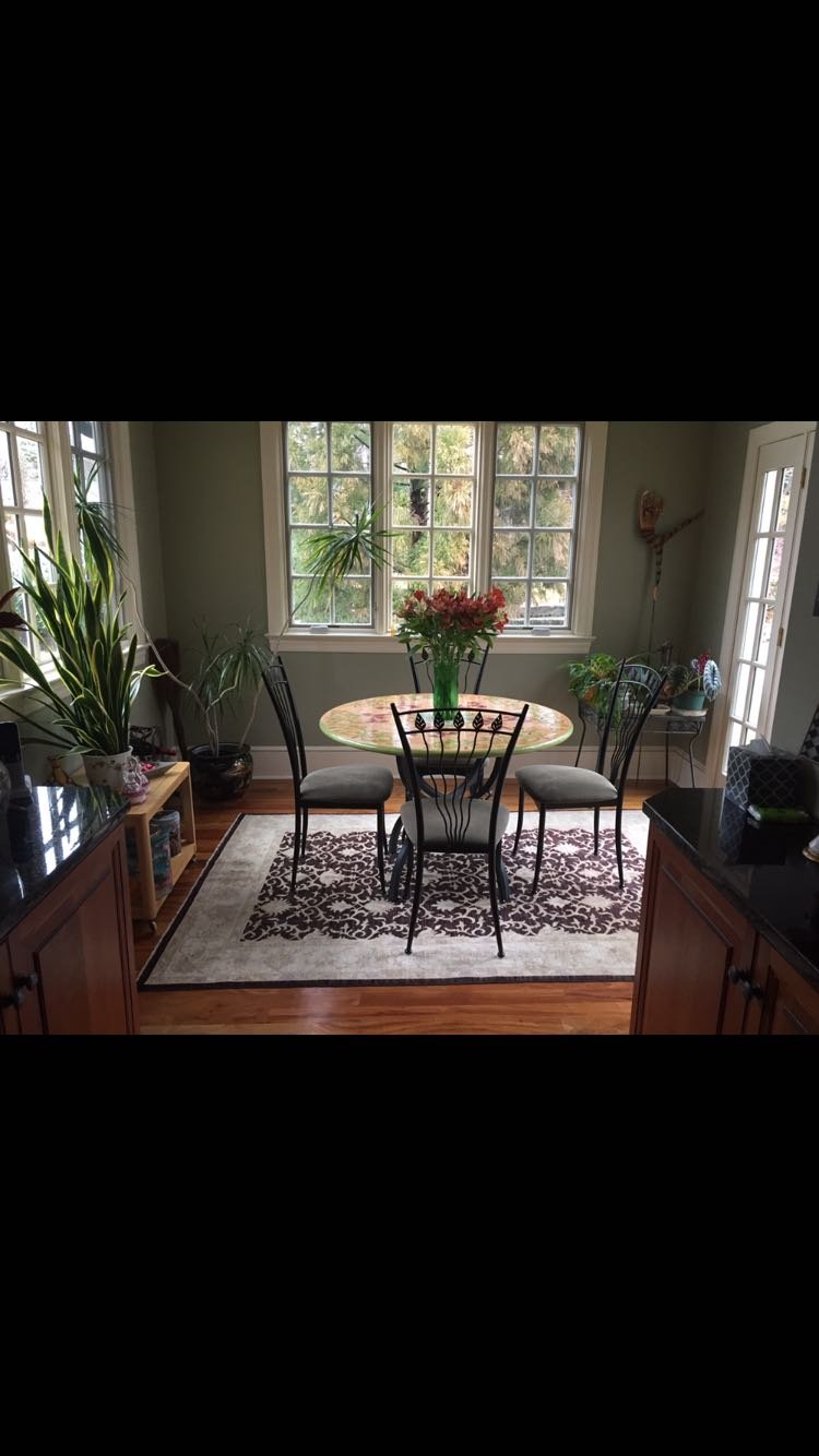 Dining room with round table, patterned rug, chairs, and plants.