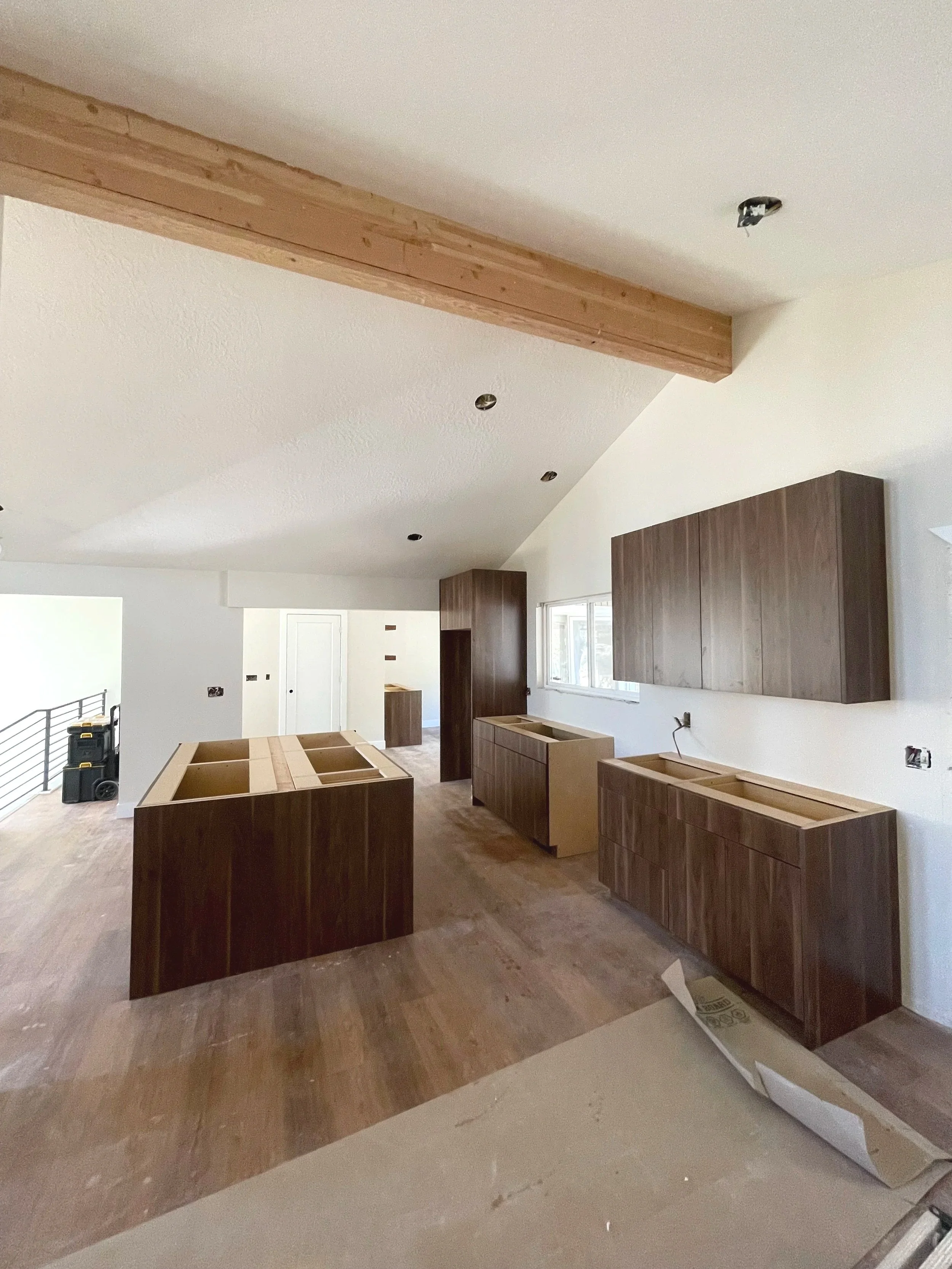Kitchen under construction with wooden cabinets and an island, unfinished countertops, and missing fixtures.