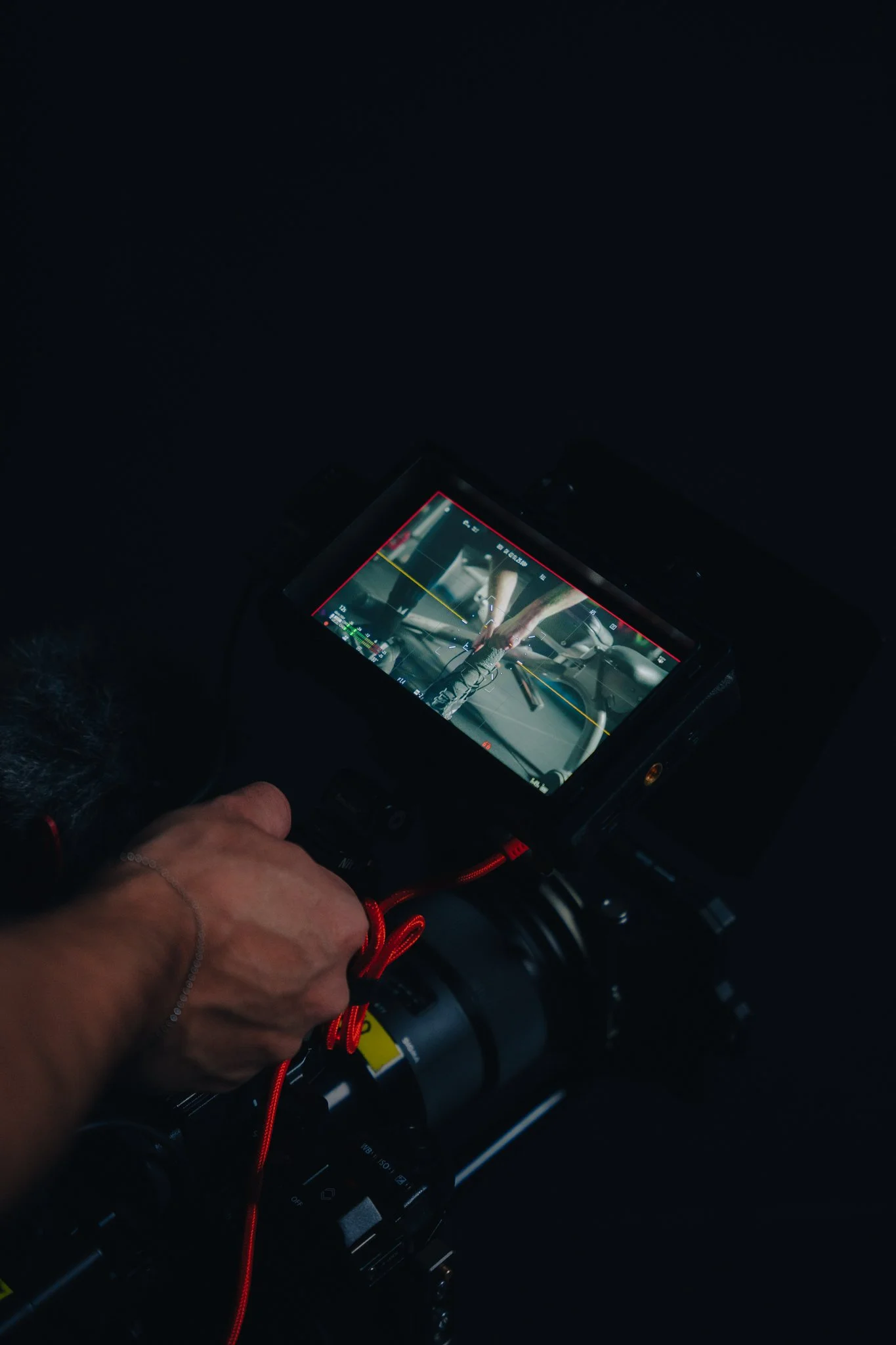 A person operating a professional camera on a tripod, capturing footage of a person working with tools, visible on the camera screen.