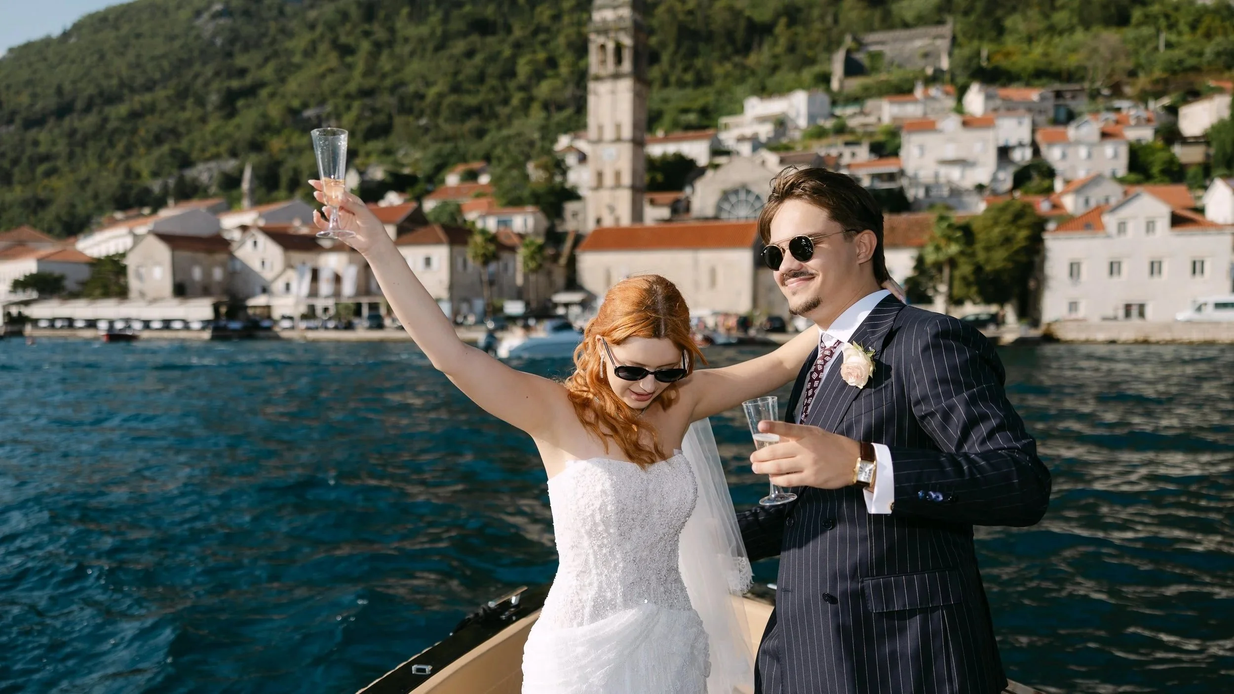 A newlywed couple enjoy their boat tour in Bay of Kotor, Perast in the background, prosecco and views