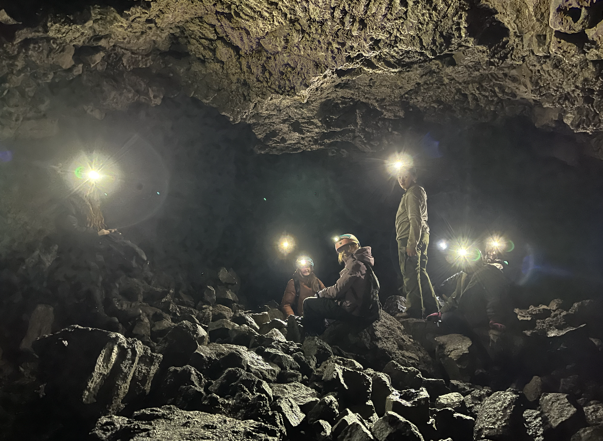 Group of people with headlamps exploring inside a dark cave with rocky ground and ceiling.