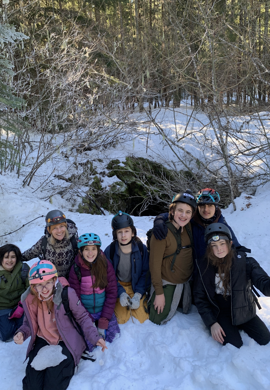 Group of children and teenagers in winter gear, smiling and posing together outdoors in a snowy forest