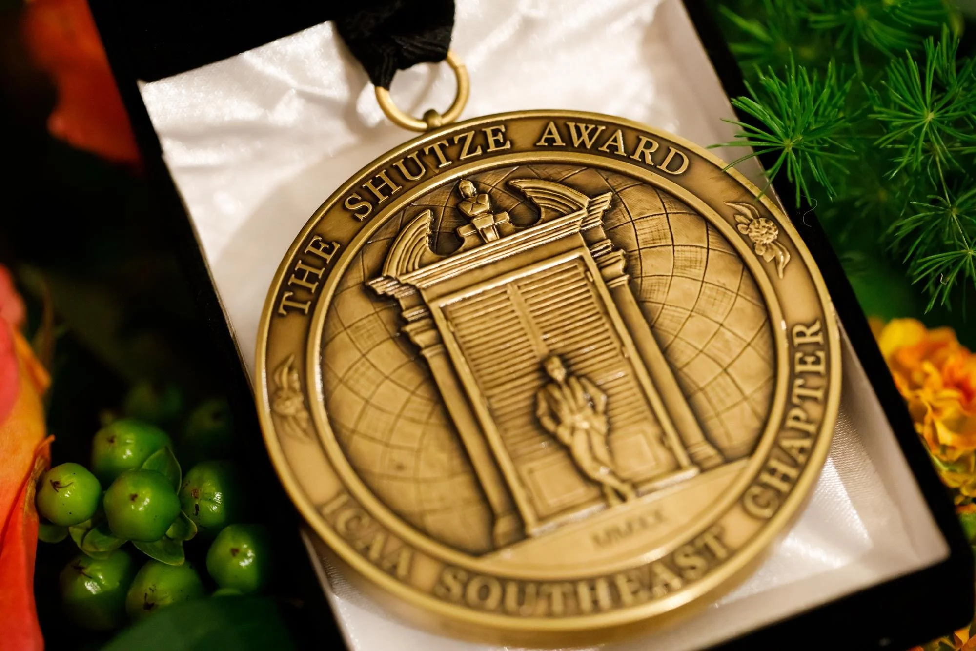 Medal with the inscription "The Schutzze Award" and a depiction of a person knocking on a door, surrounded by greenery and flowers.
