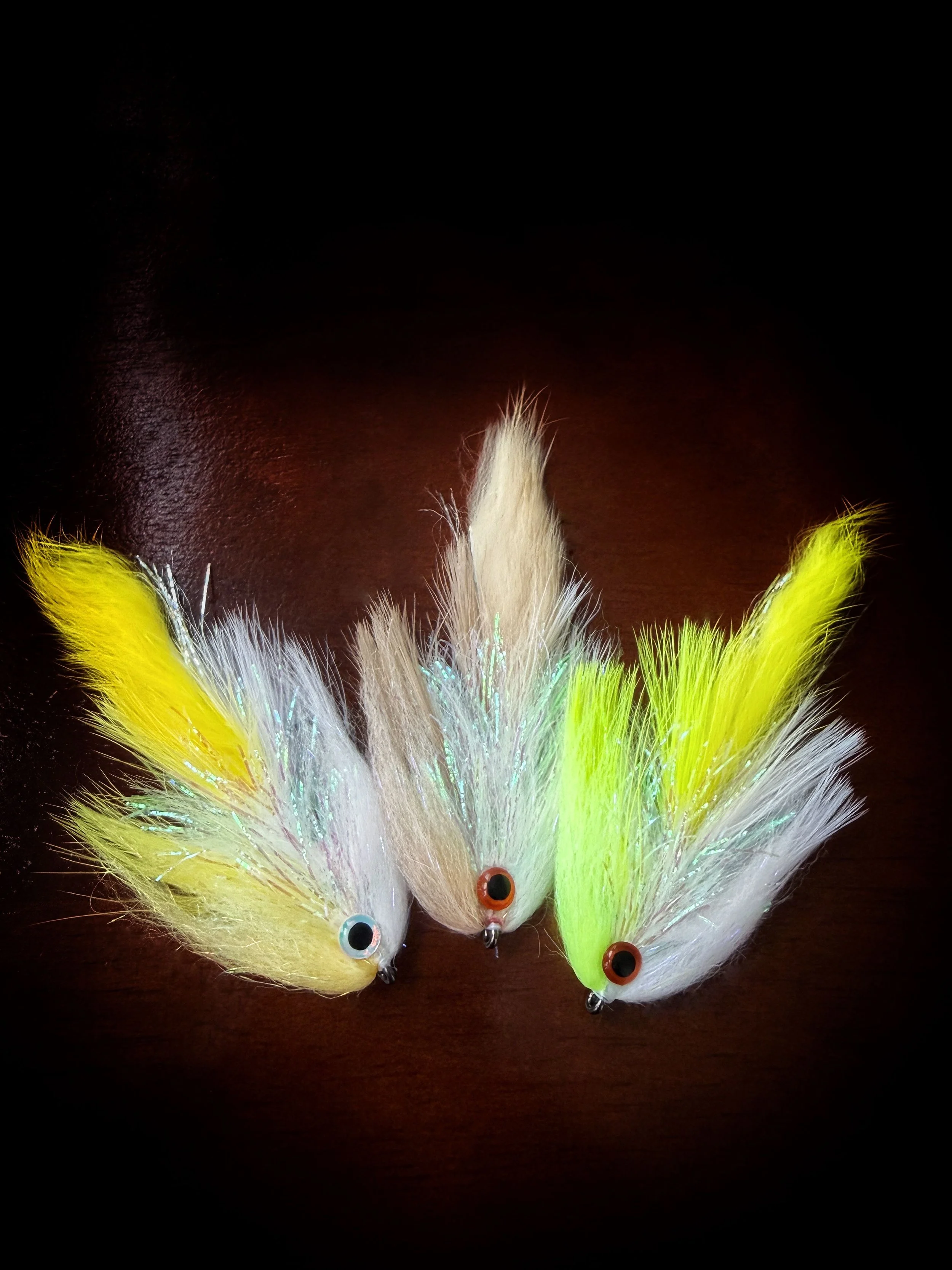 Collection of colorful fishing lures with feathers and plastic eyes on a dark surface.