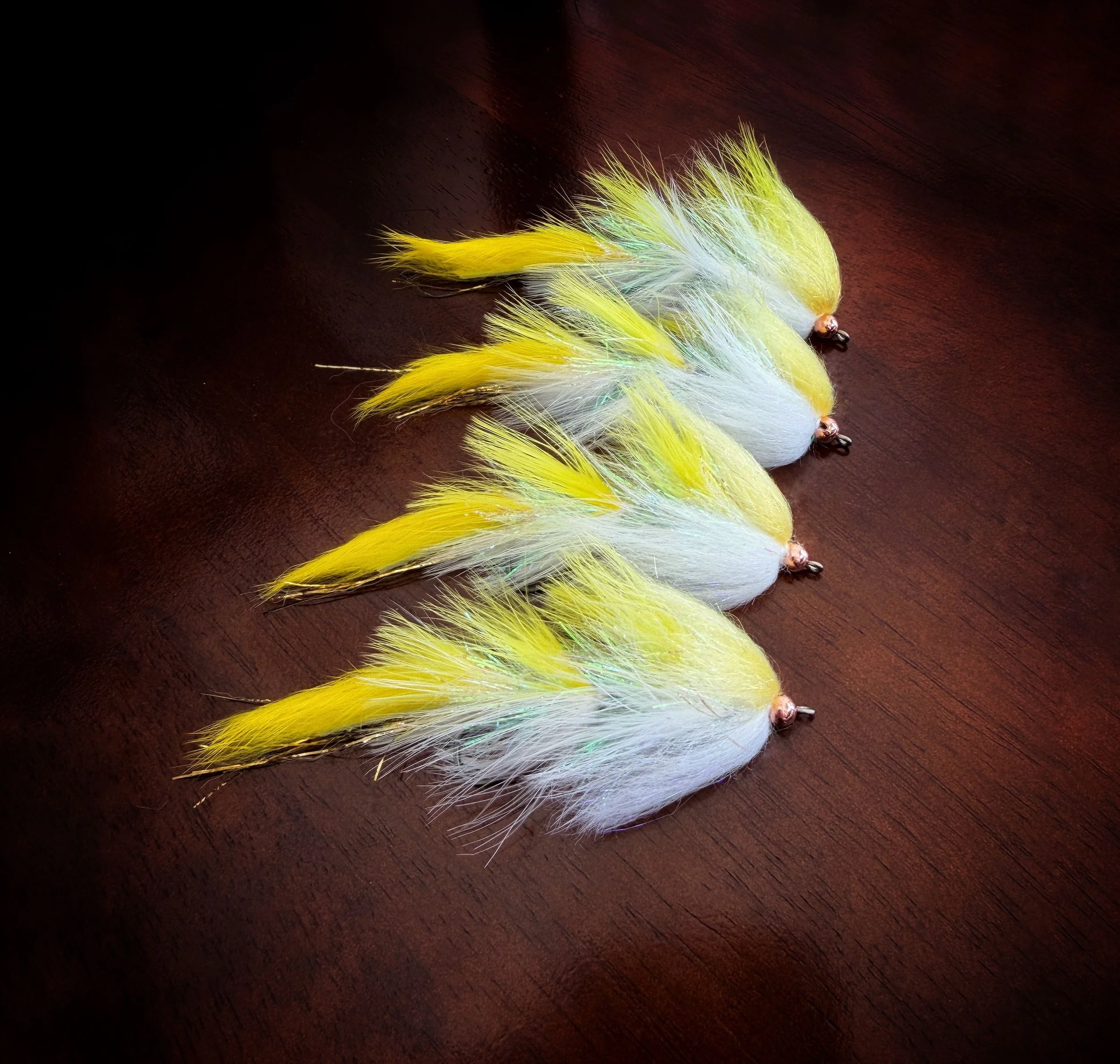 Four fishing lures with white and yellow feathers aligned on a wooden surface.