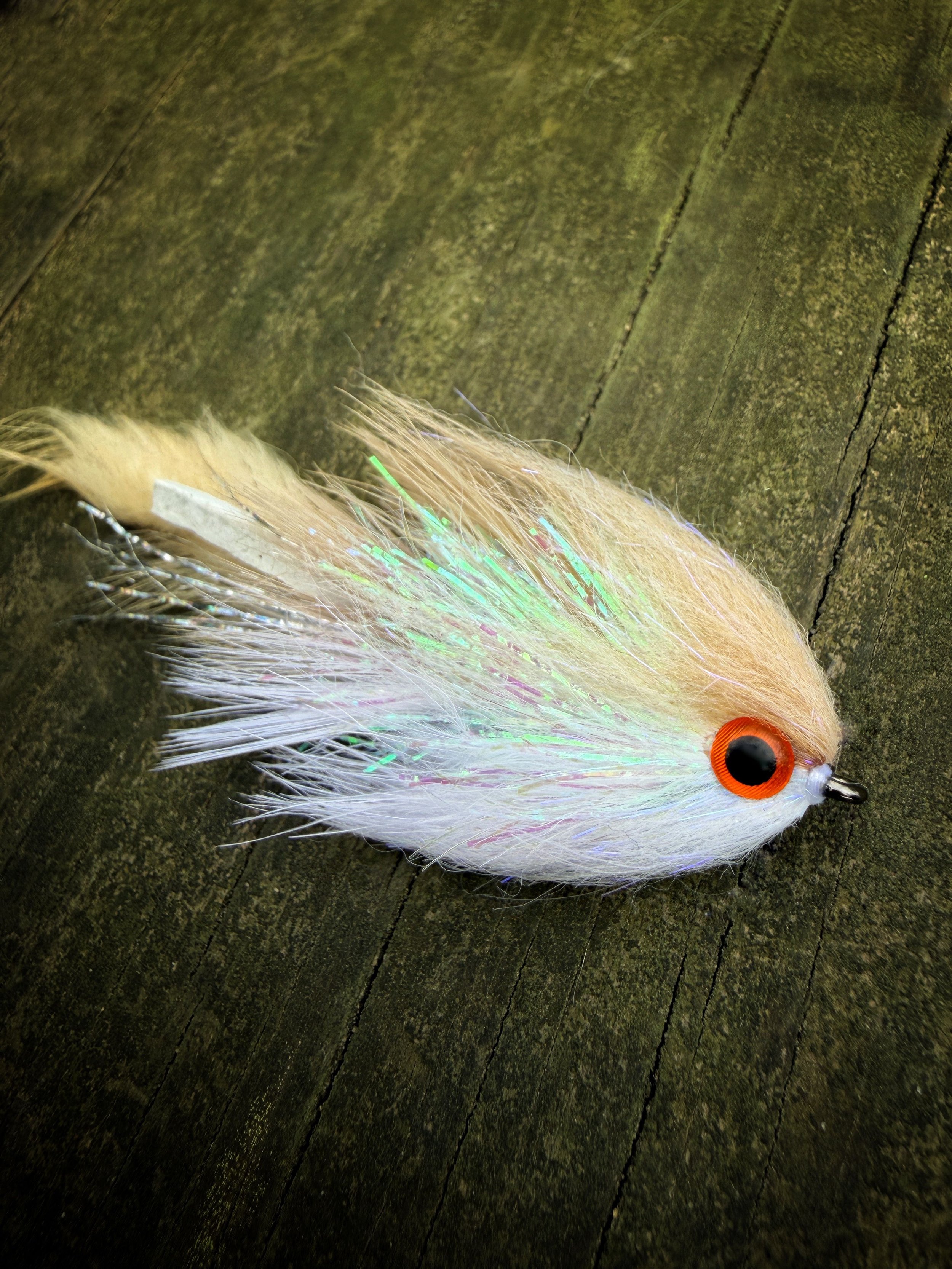 A fishing lure with a plush, flowing tail and iridescent accents, resting on a weathered wooden surface.