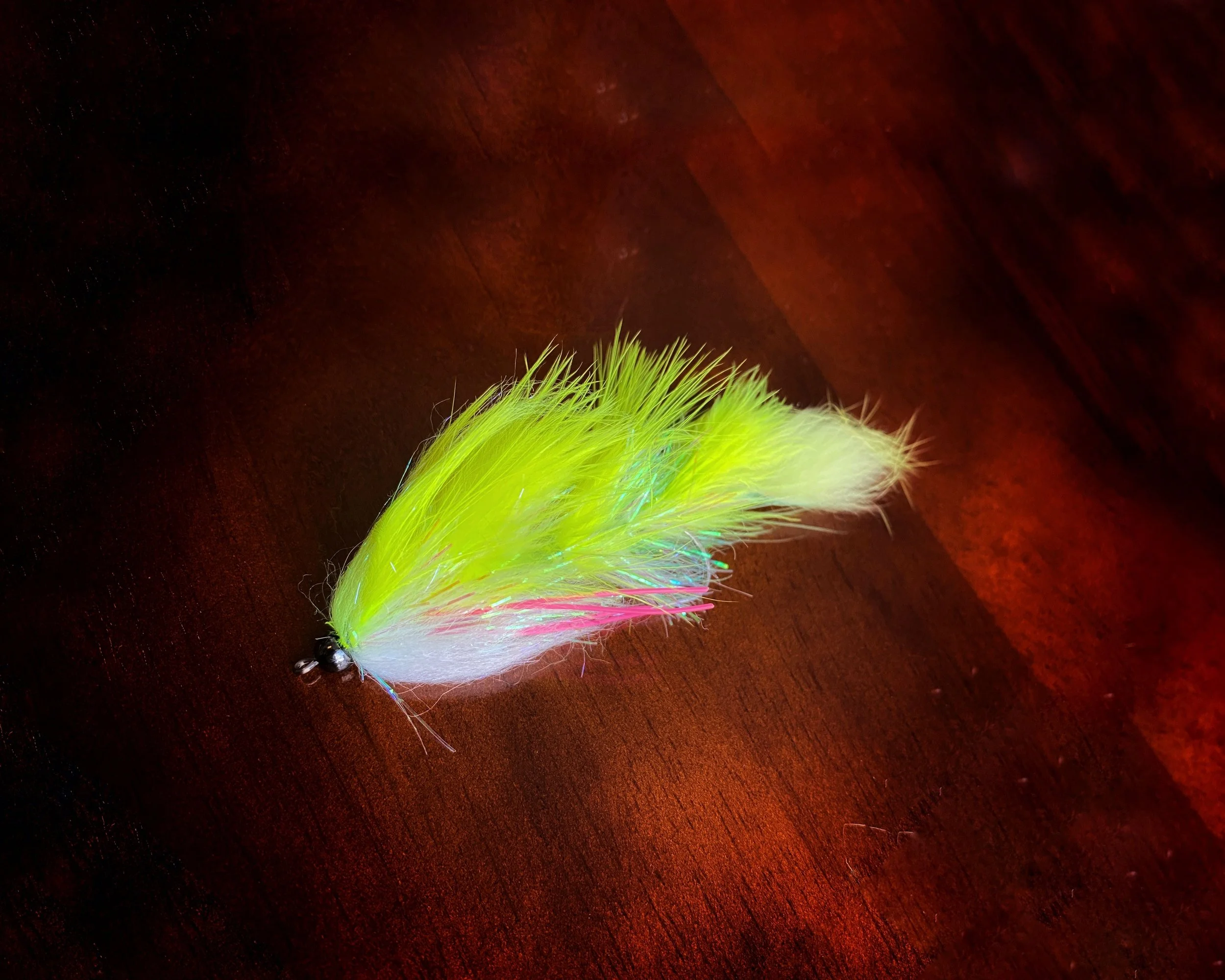Bright yellow and white fishing lure with iridescent strands resting on a wooden surface.