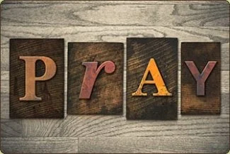 The word "PRAY" spelled with wooden letter blocks on a wooden surface.