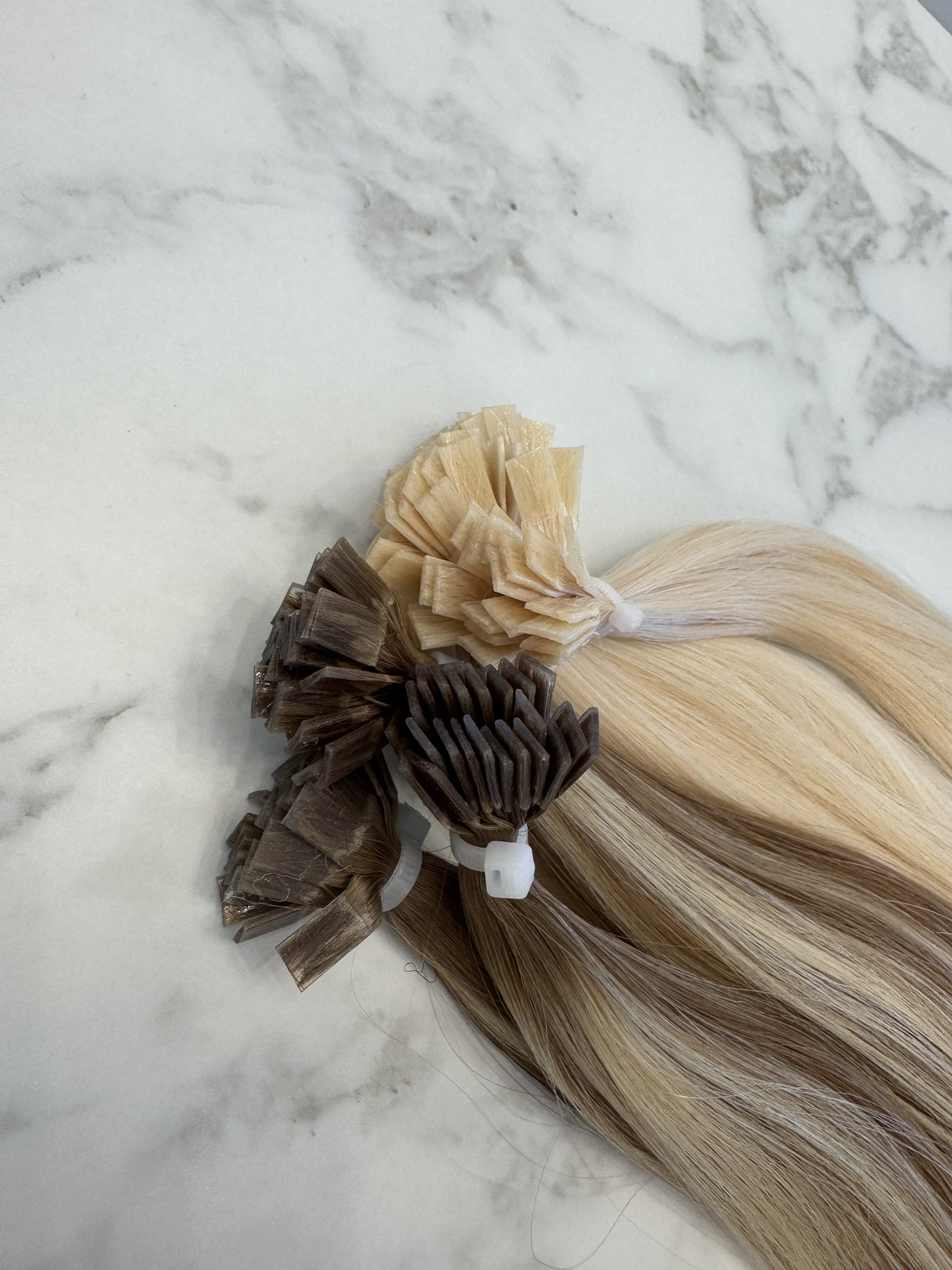 Keratin bond hair extensions in multiple shades laid flat on marble, bundled in flat tips for salon installation.