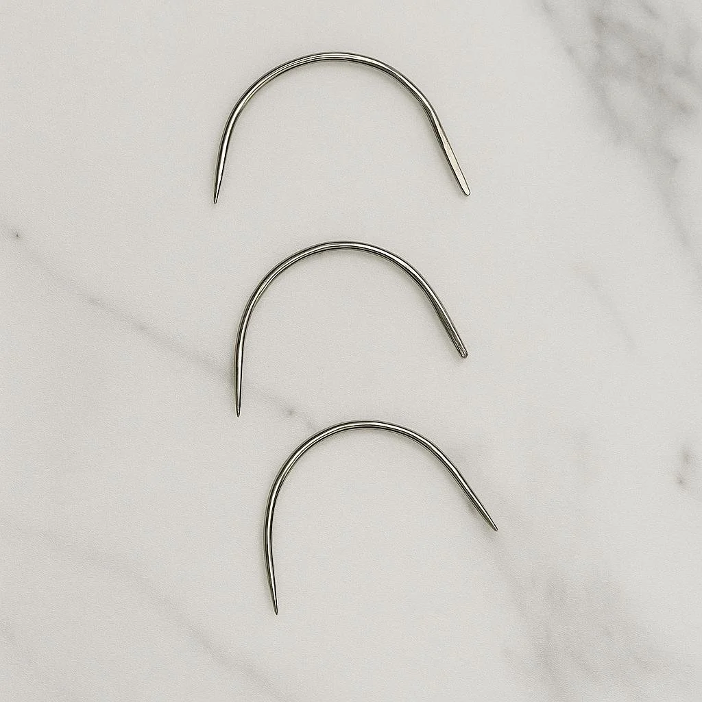 Three curved sewing needles laid out on a marble surface, used for hair extension application.