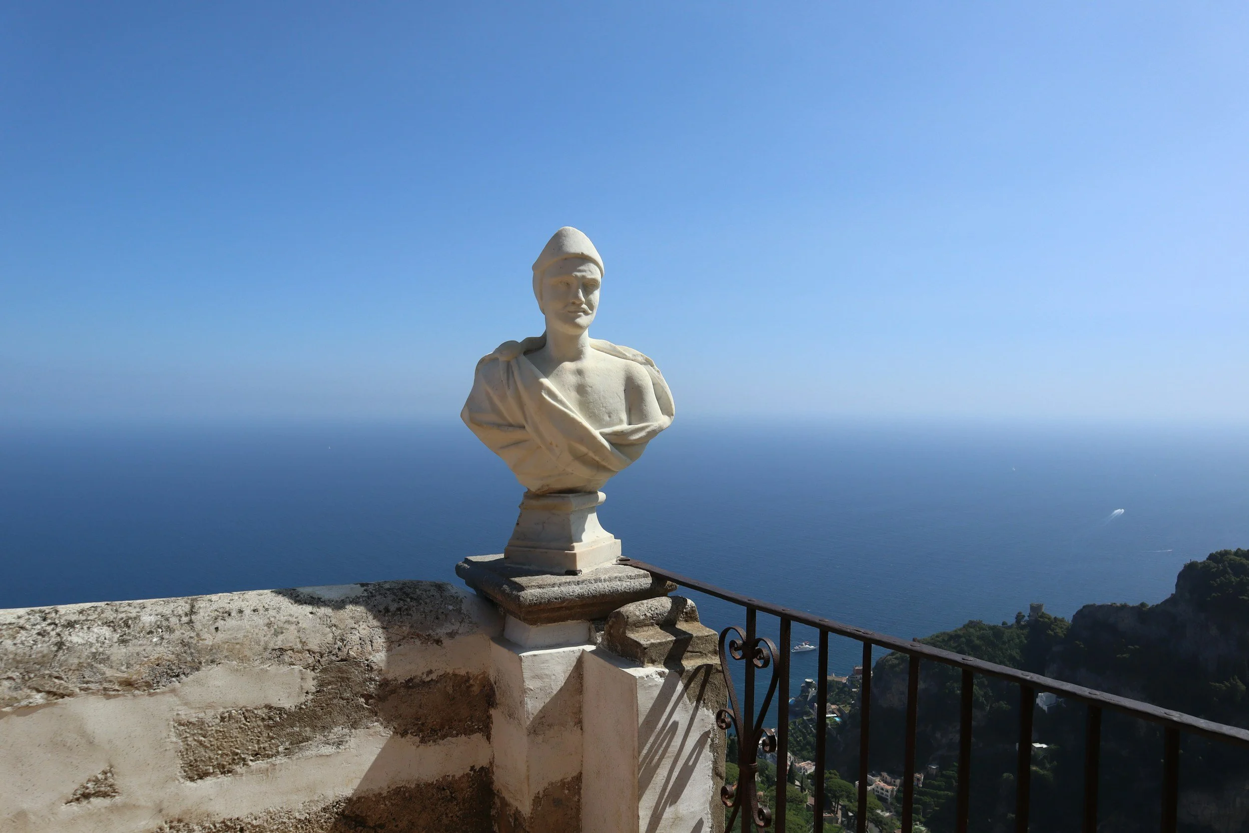 Reset Retreat in Italy. Statue of a woman in a military uniform, overlooking a coastal landscape with the sea and distant islands under a clear blue sky.