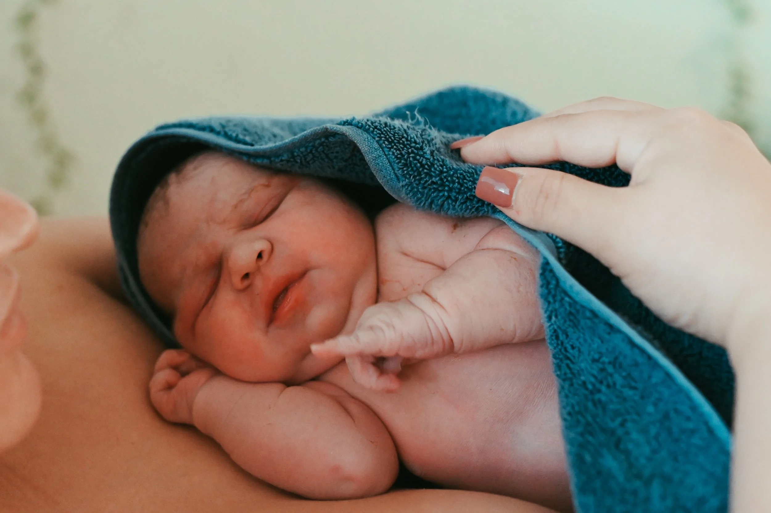 A newborn baby wrapped in a blue towel, lying on her mother's chest, with the mother holding the baby gently. The baby's eyes are closed, and it looks peaceful and content. In Austin, Texas.