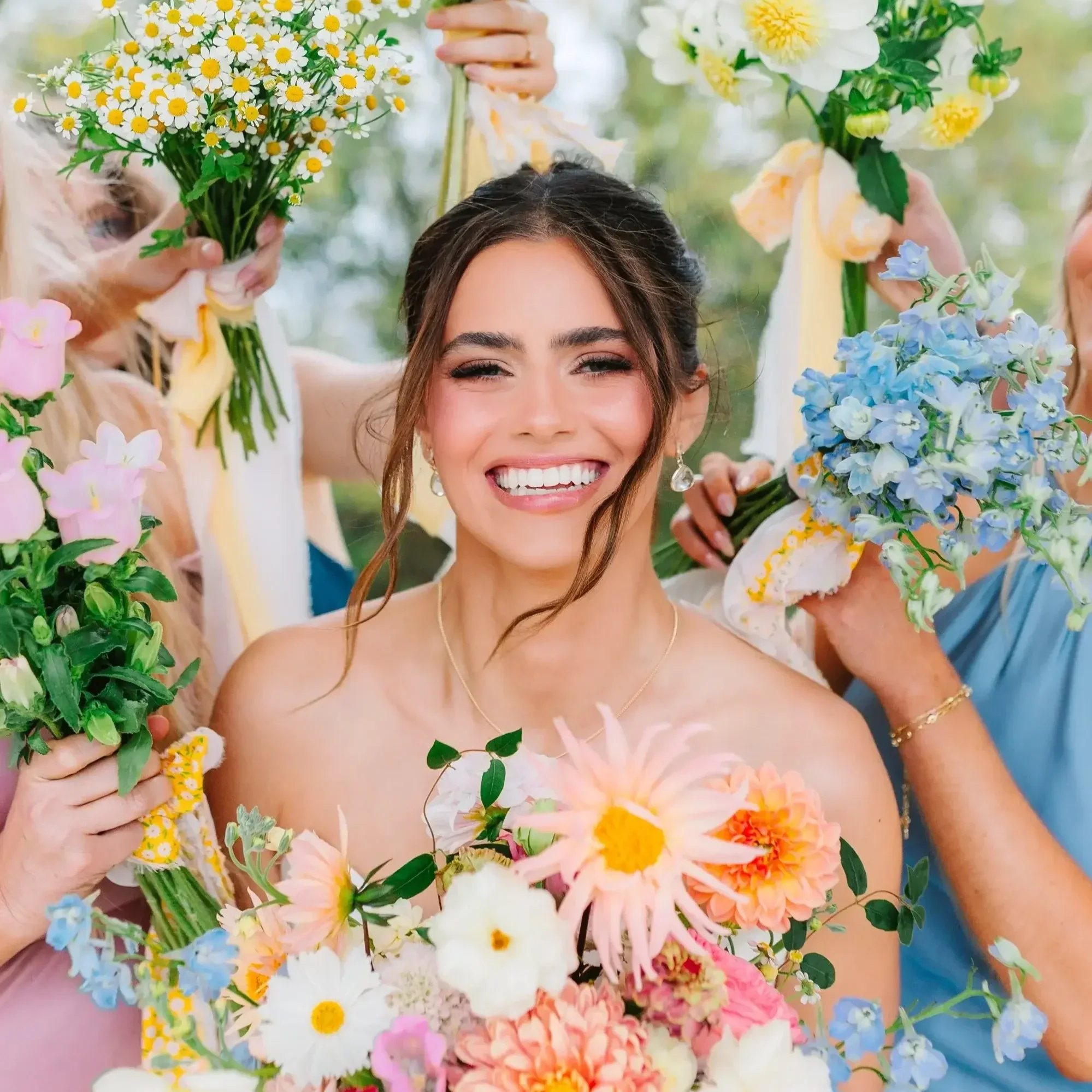 A smiling woman with dark hair and earrings surrounded by and holding colorful flowers at a celebration.