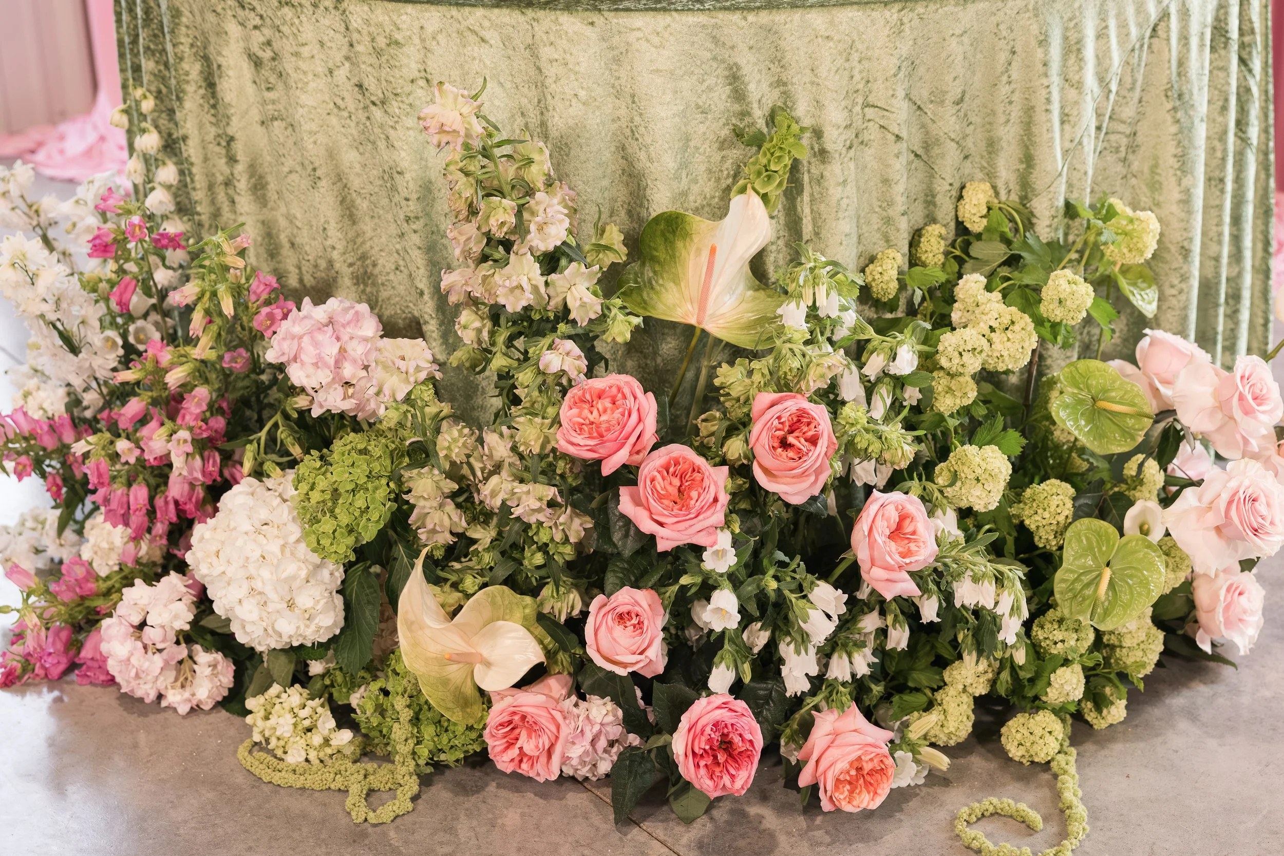 Arrangement of pink and white flowers with greenery against a green velvet backdrop.