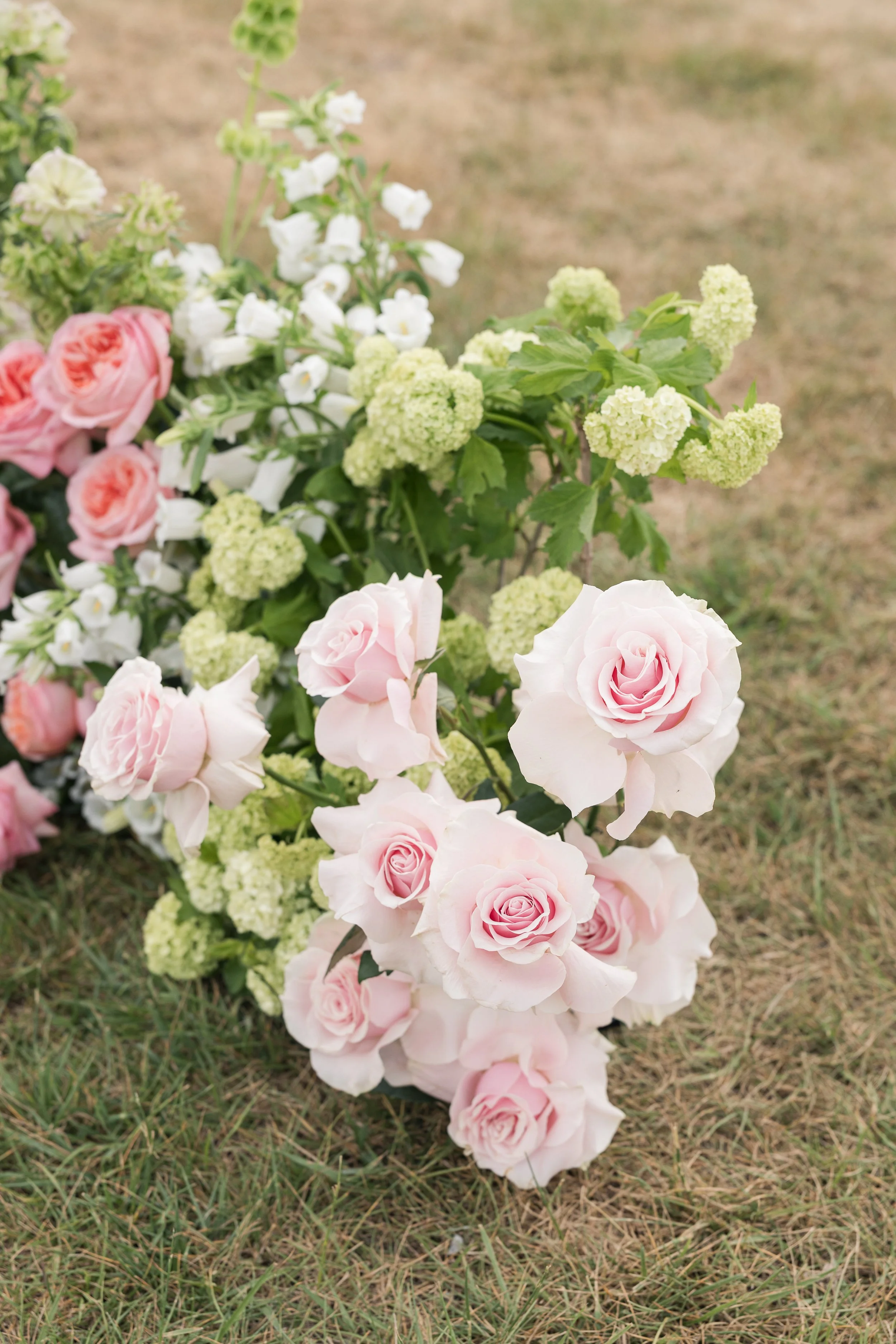 A colorful array of flowers lying on the grass, including pink roses, white carnations, and green hydrangeas.