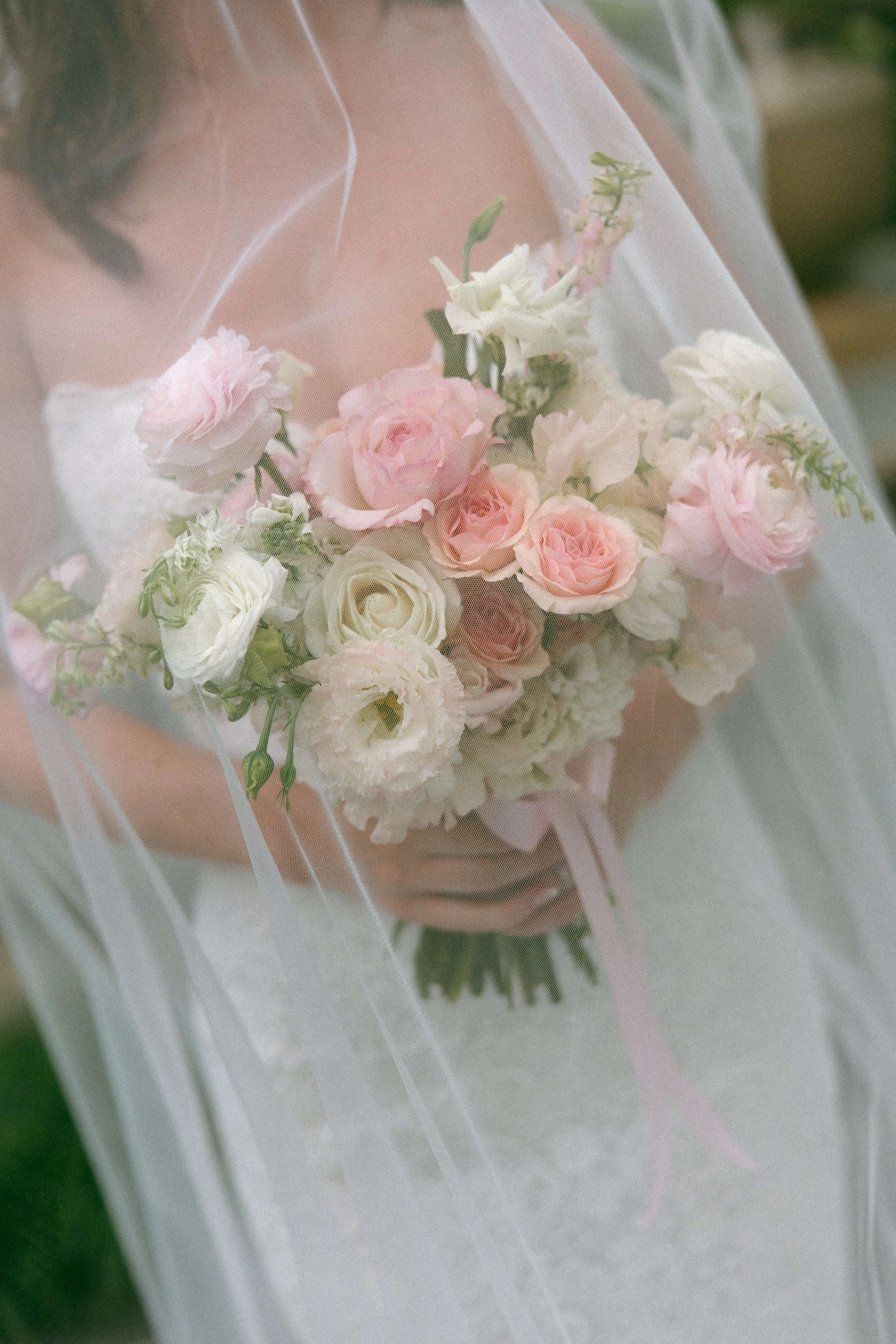 Close-up of a bride holding a bouquet of pink and white roses, with a soft-focus background.