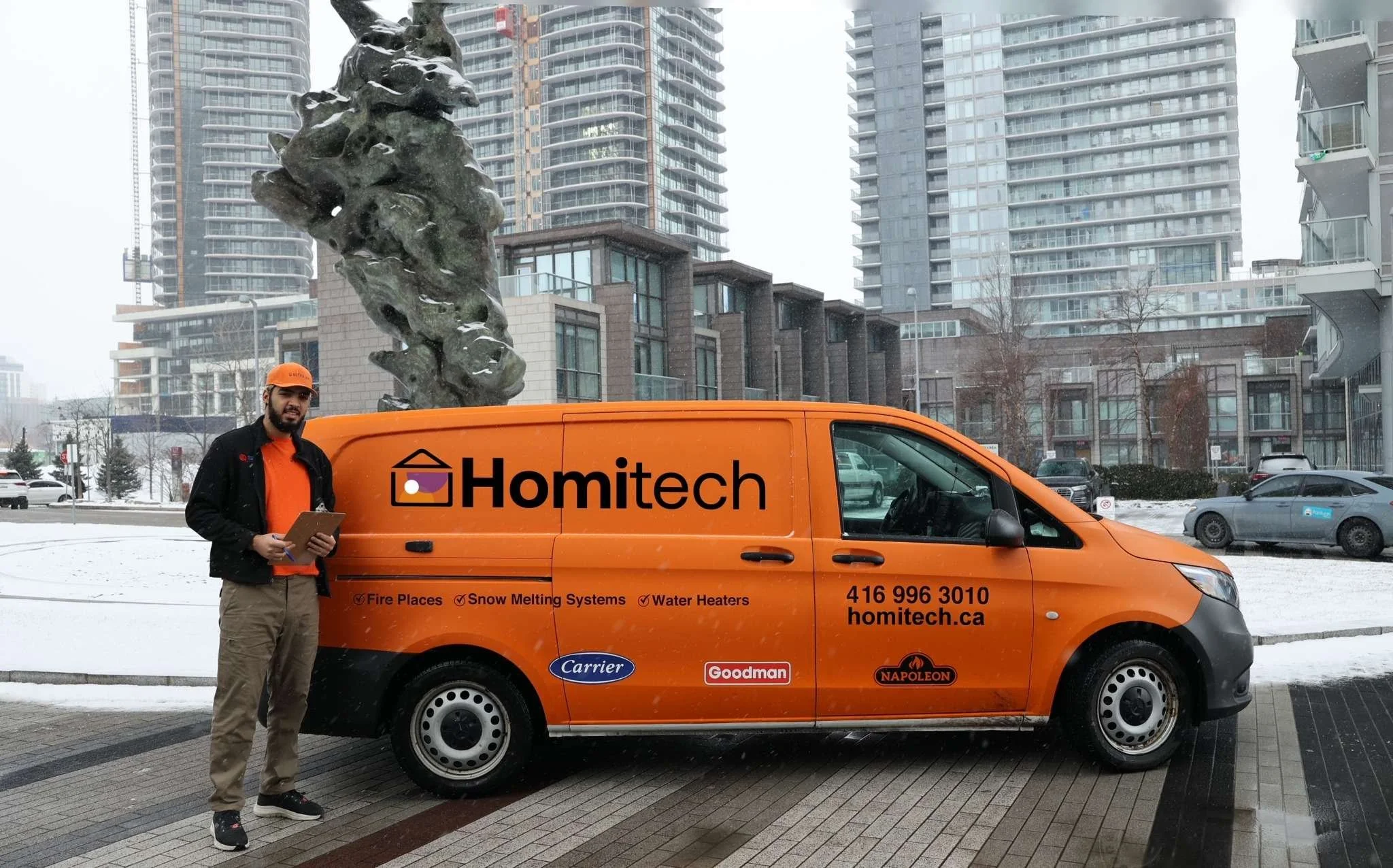Orange van with "Homitech" branding parked on snowy street, person standing beside it holding a clipboard, with tall buildings in the background.