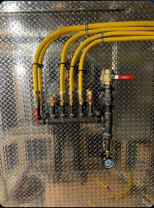 A set of yellow flexible gas lines connected to a metal manifold with valves on a diamond plate metal background.