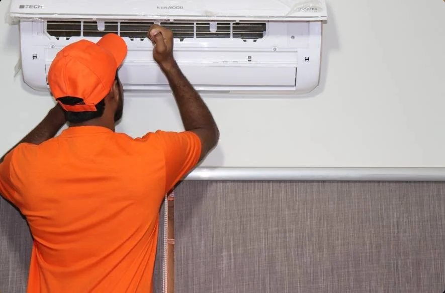 Person repairing a wall-mounted air conditioner wearing an orange cap and shirt.