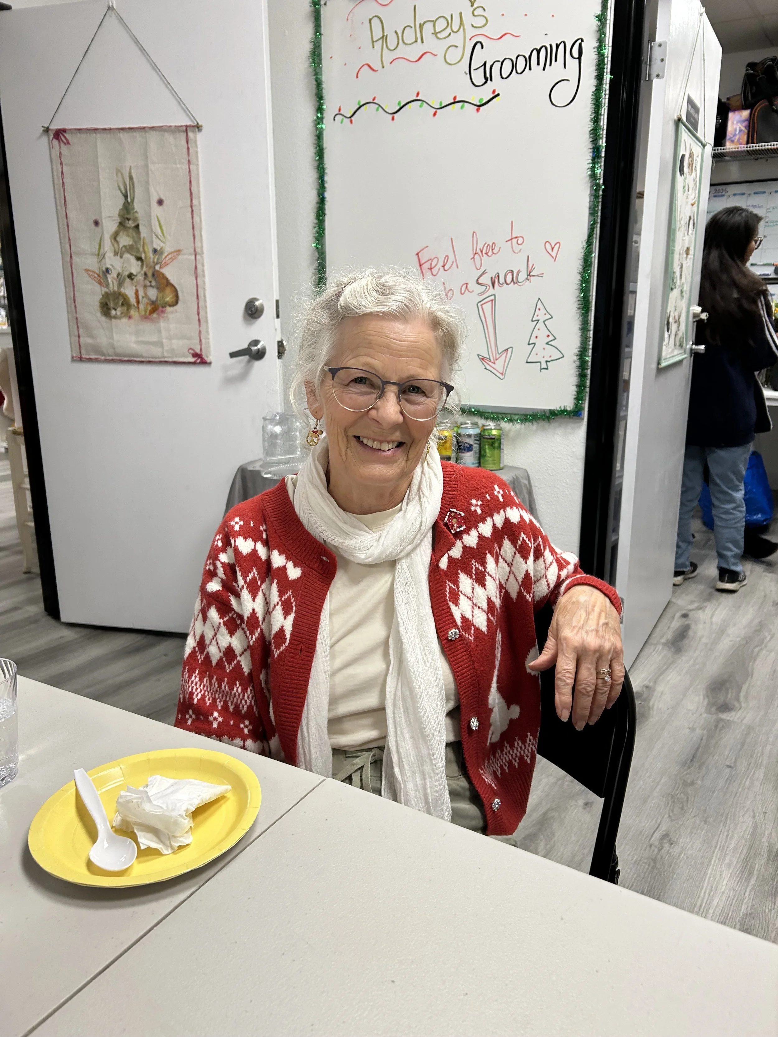 Photo of seated woman with red sweater, white scarf, and glasses.