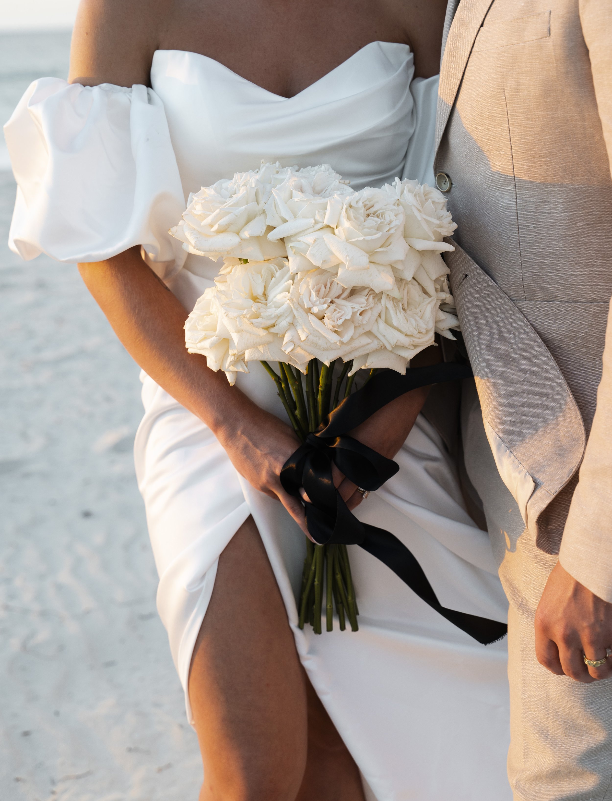 Bride and groom holding a bouquet of white roses on a beach.