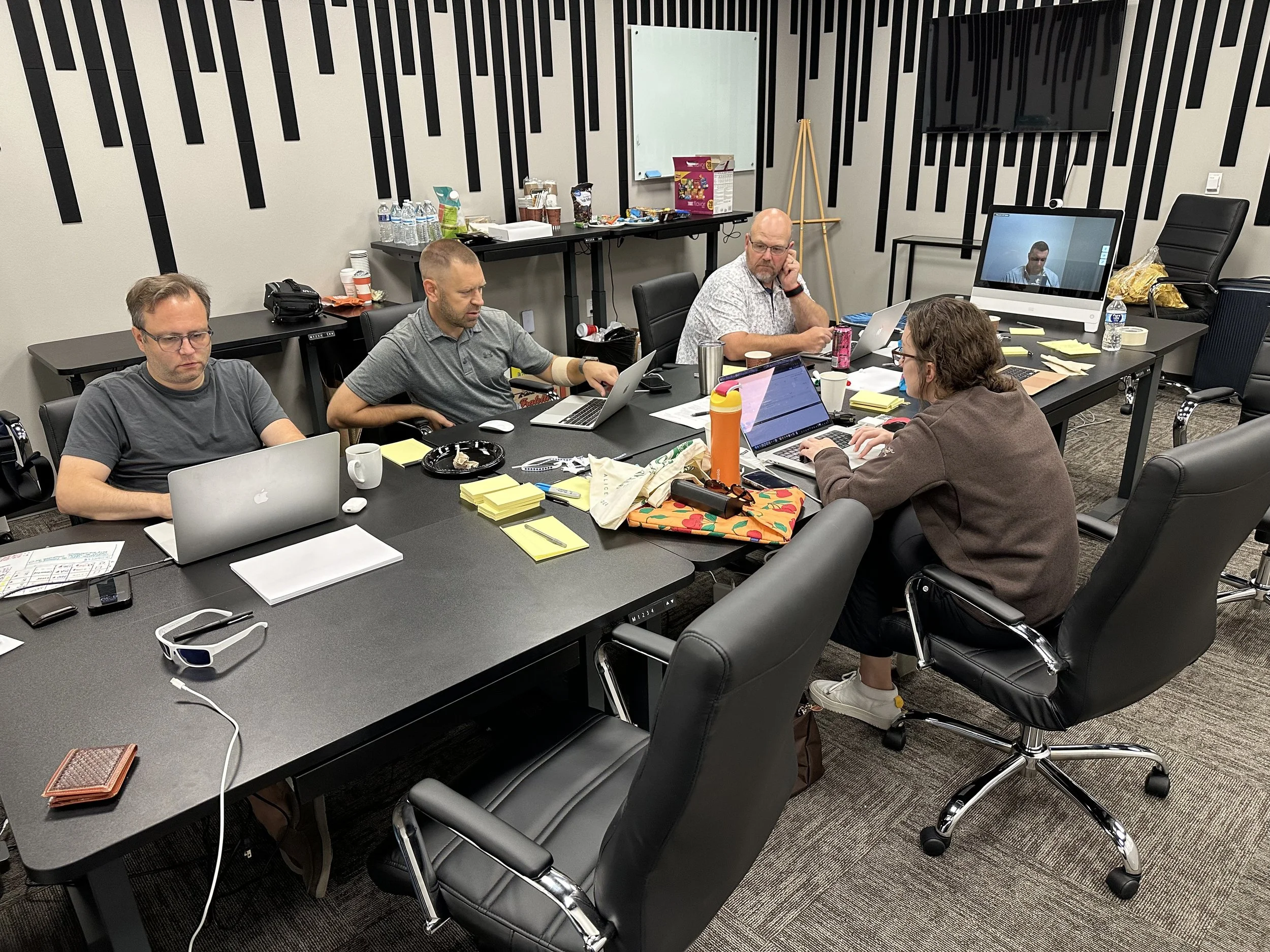 Four people working on laptops at a conference table in a modern office meeting room with black and white decor.