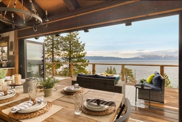 Covered outdoor dining deck with set table, fire pit seating, and panoramic Lake Tahoe view at dusk
