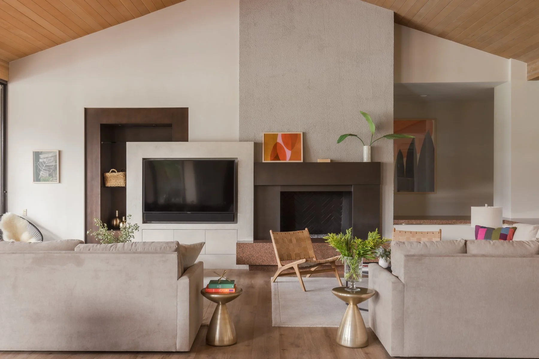 Modern living room with beige sofas, a flat-screen TV, a fireplace, and decorative plants and artwork.