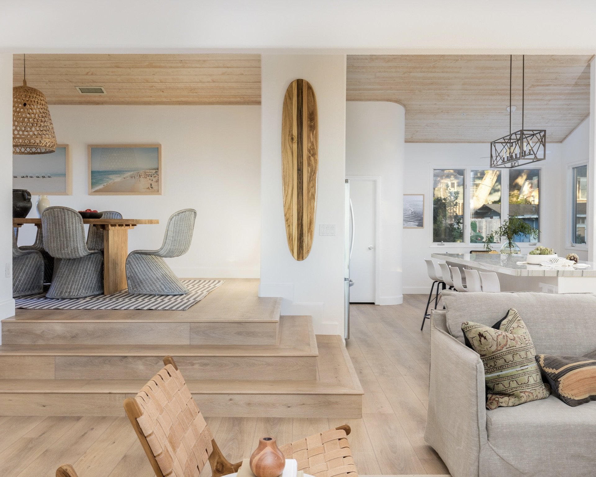 Open-concept living and dining area with wooden accents, light-colored furniture, and large windows letting in natural light.