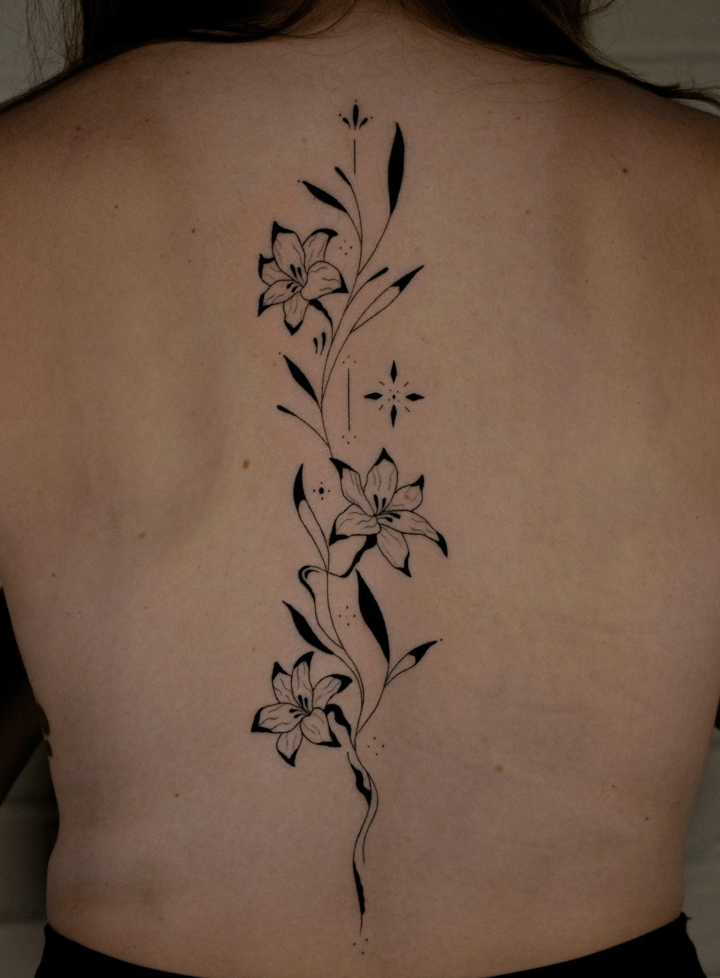 Fine Line floral / flowers tattoo on the spine - this minimalist black work style was created by Erica Inagaki in Arvada Colorado.