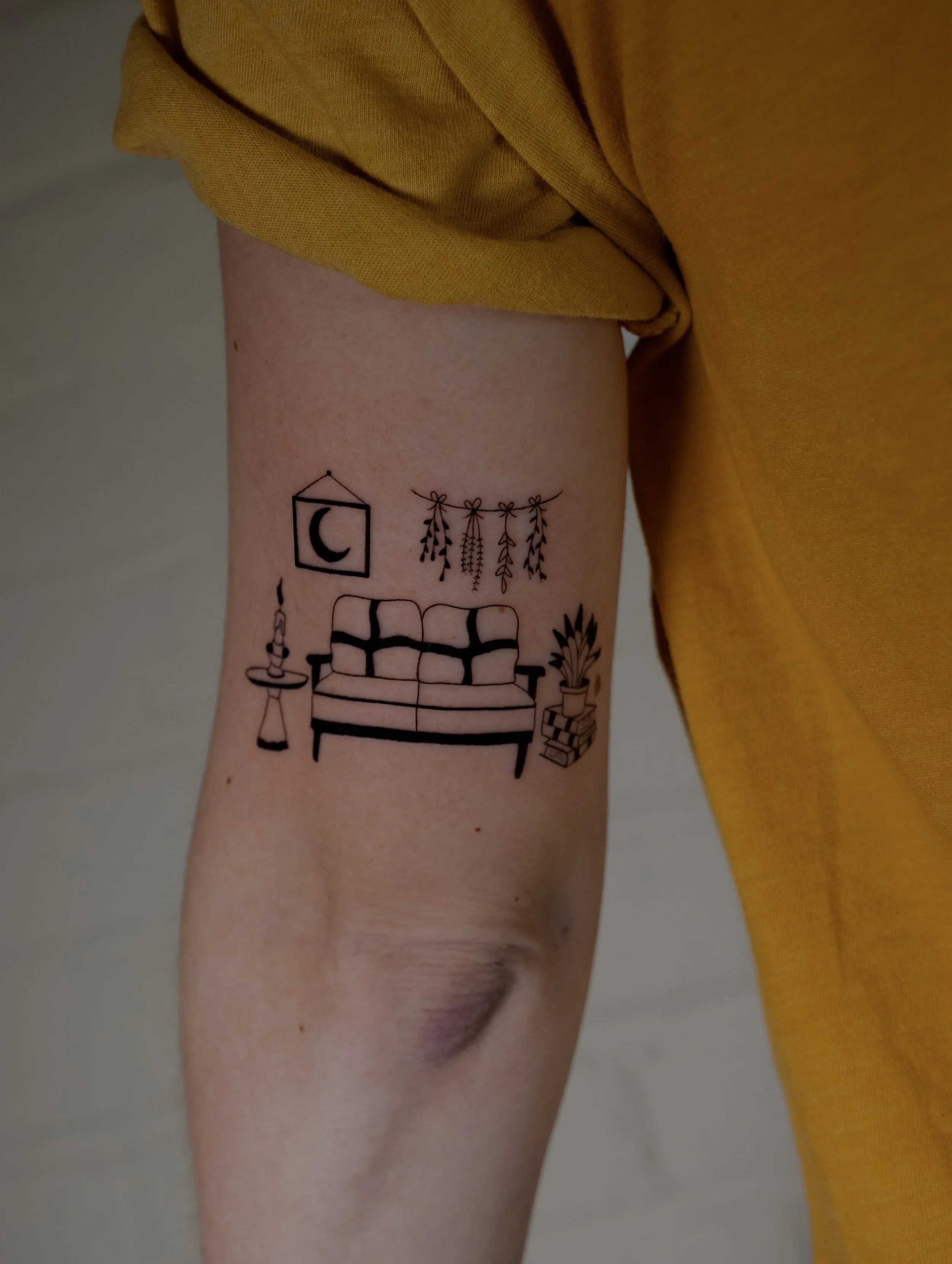 Minimalist living room tattoo, small fine line tattoo that depicts a living room including a sofa, plants and wall decor in a small format on the arm. Small fun tattoos created by Erica Inagaki in Lake Wood Colorado