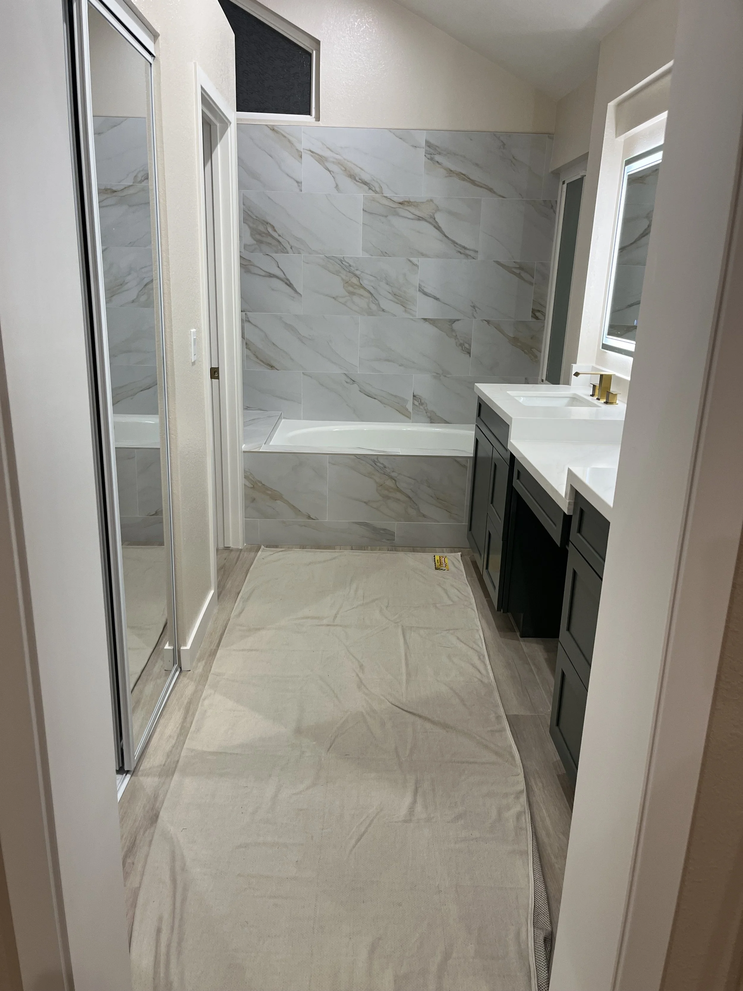 Modern bathroom with marble tile wall, bathtub, vanity with double sink, mirror, and shower with sliding glass door, beige carpet on the floor.