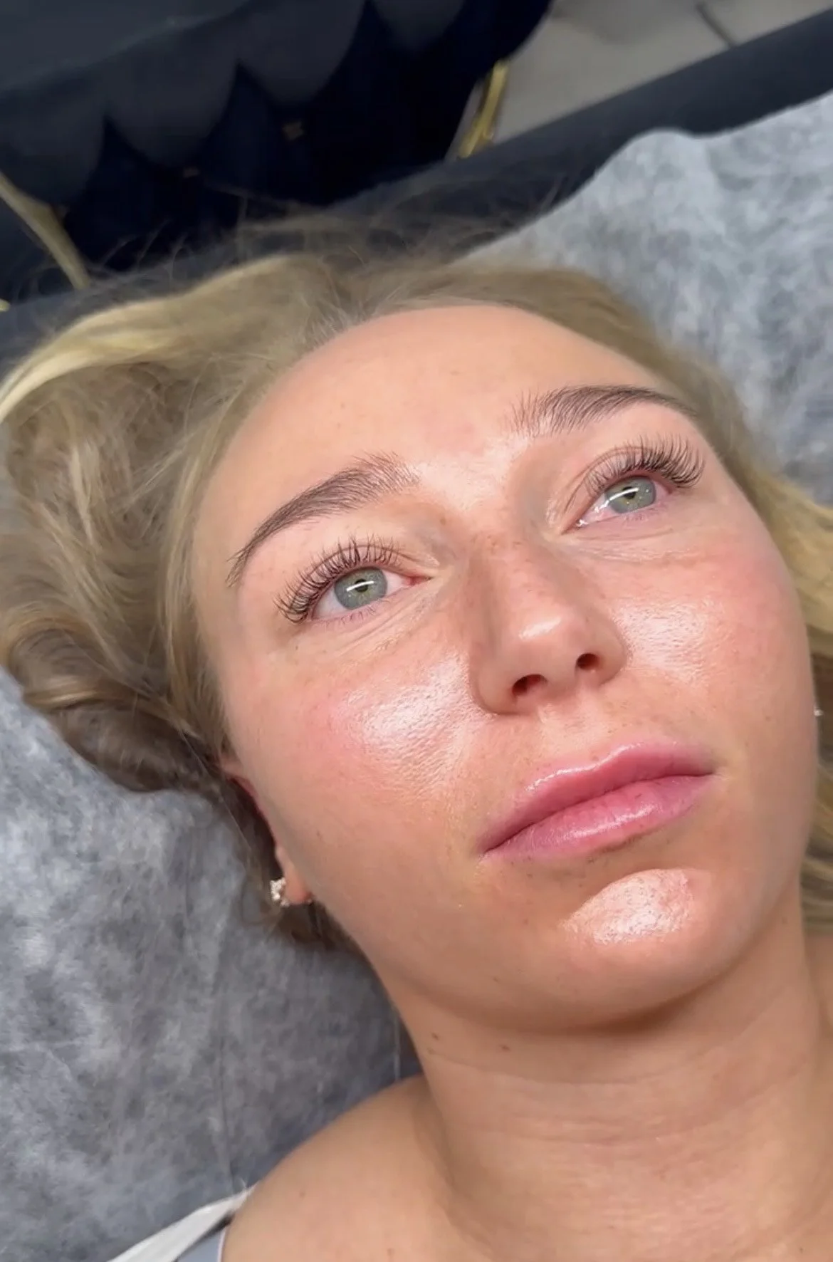 Nærbilde av en kvinne med blond hår, lyse hud, store øyne og rosa lepper, som ligger på en gray pute.