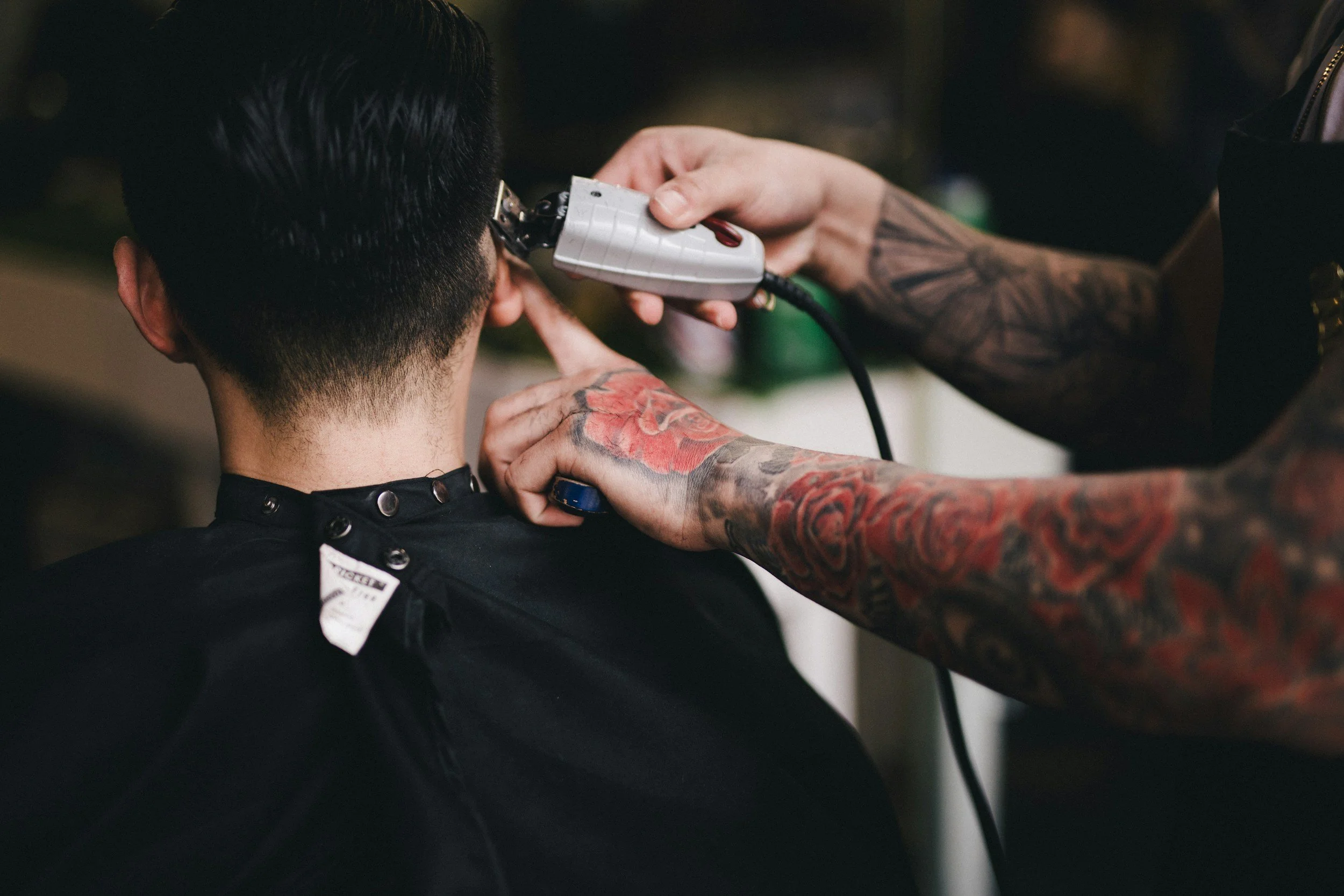 Tattooed barber giving a haircut to a client with a clippers in a salon.