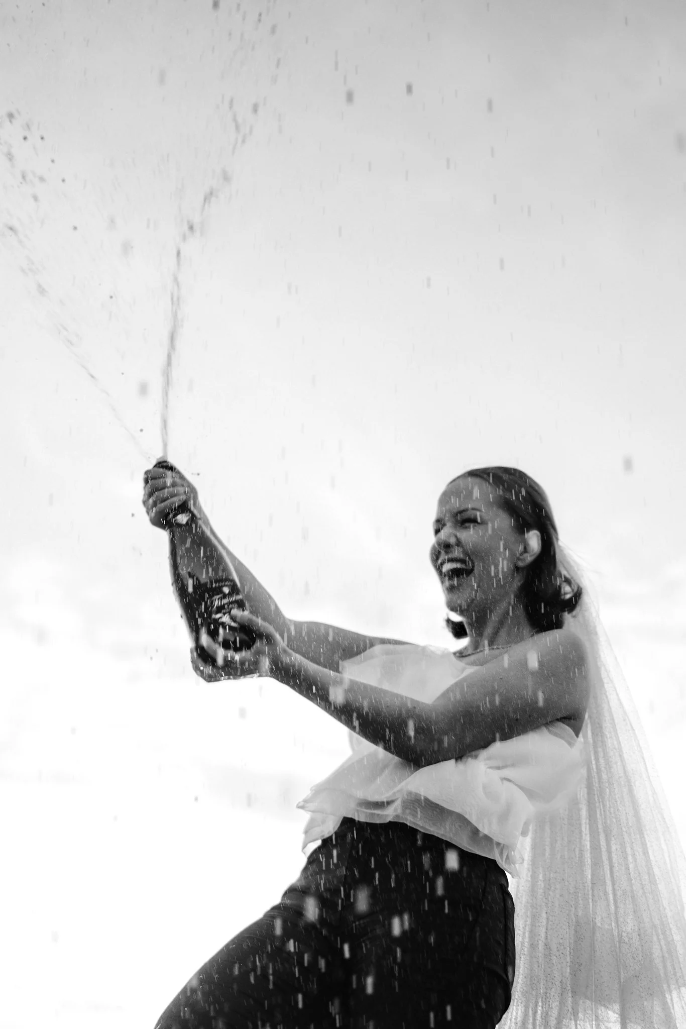 En kvinne jubler mens hun sprayer champagne i en svart-hvitt bilde.