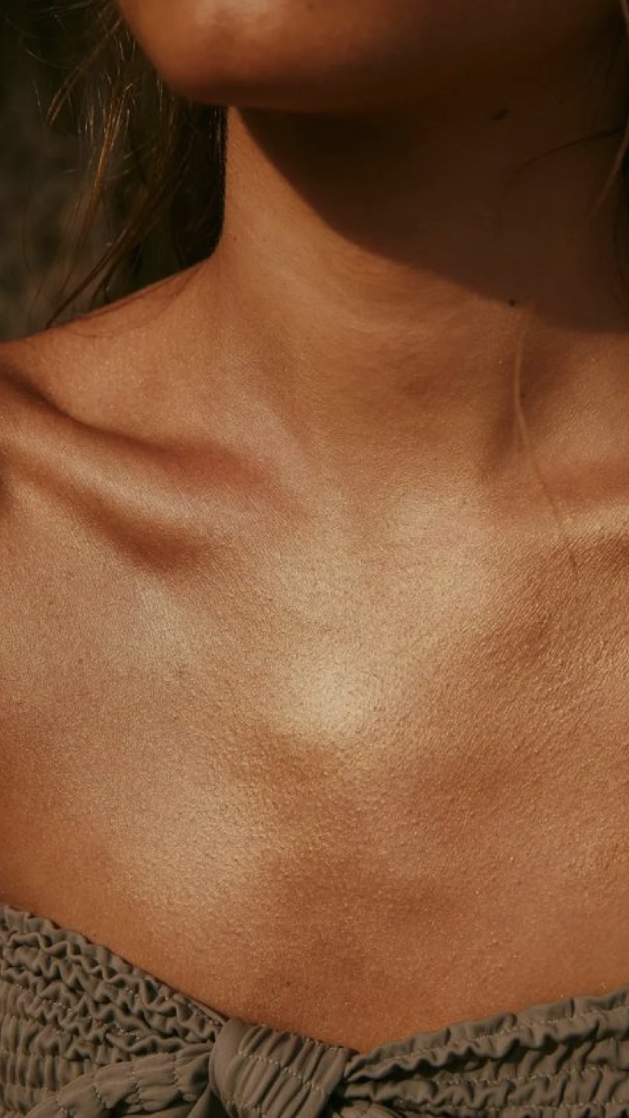Close-up of a person's neck and upper chest area, showing smooth, tan skin after a flawless spray tan at Bronze Couture in Kalamazoo, Michigan spray tanning and teeth whitening.