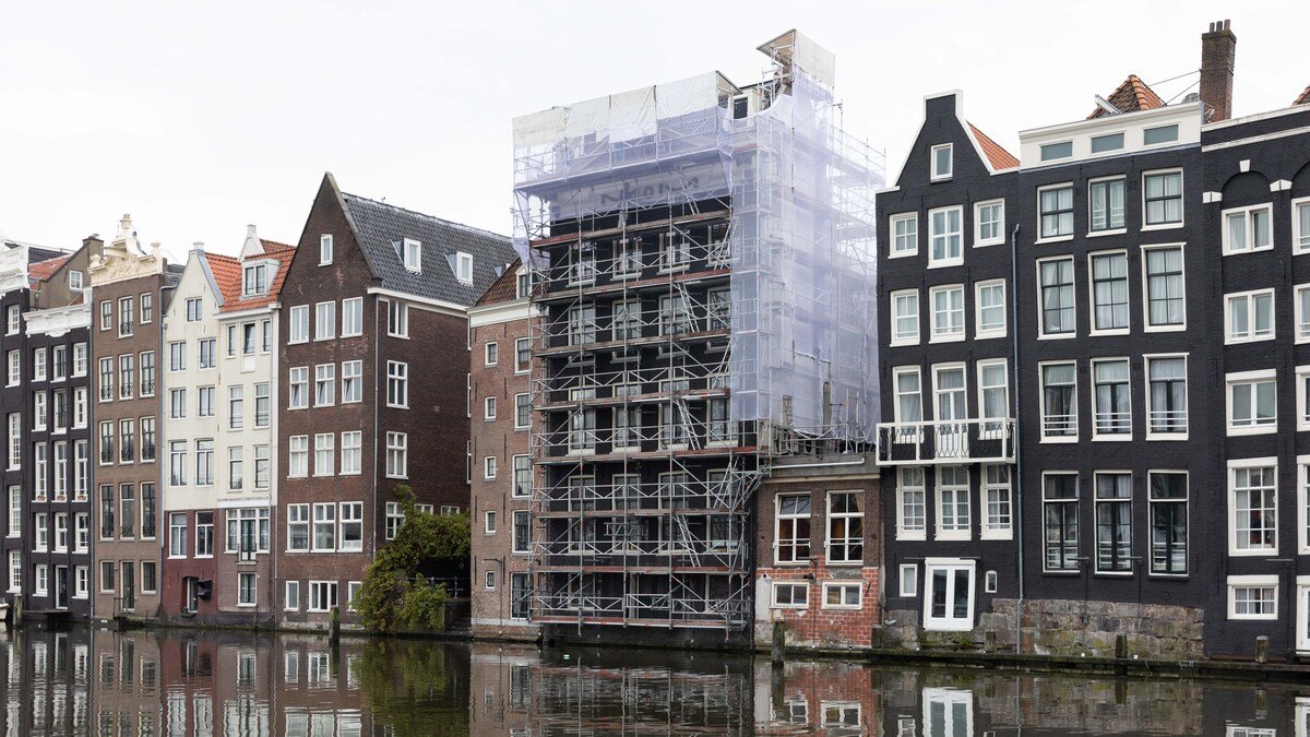 Row of traditional Dutch canal houses with construction scaffolding on a building, reflecting in water, Amsterdam.