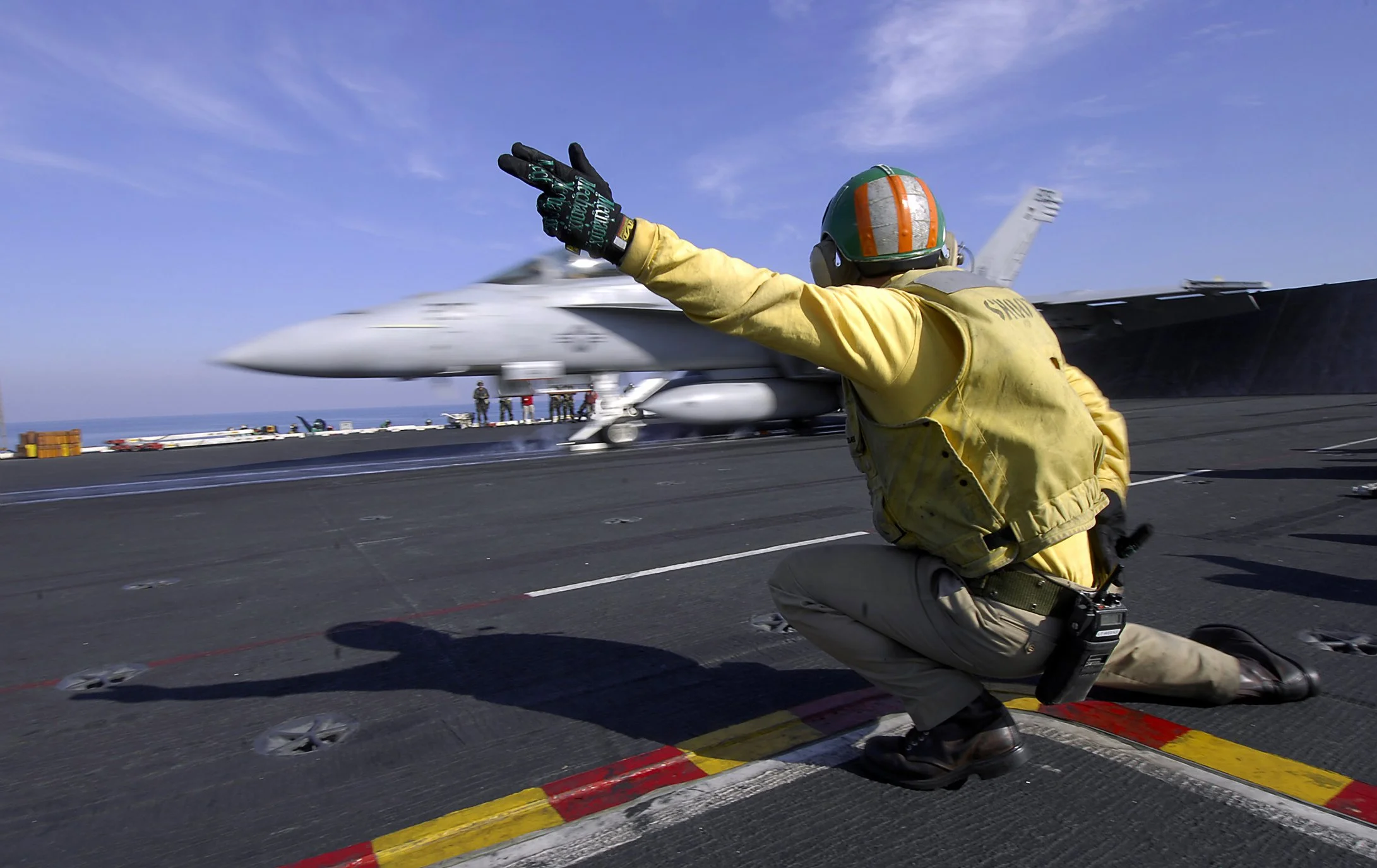 A shooter guiding an FA-18 off an aircraft carrier