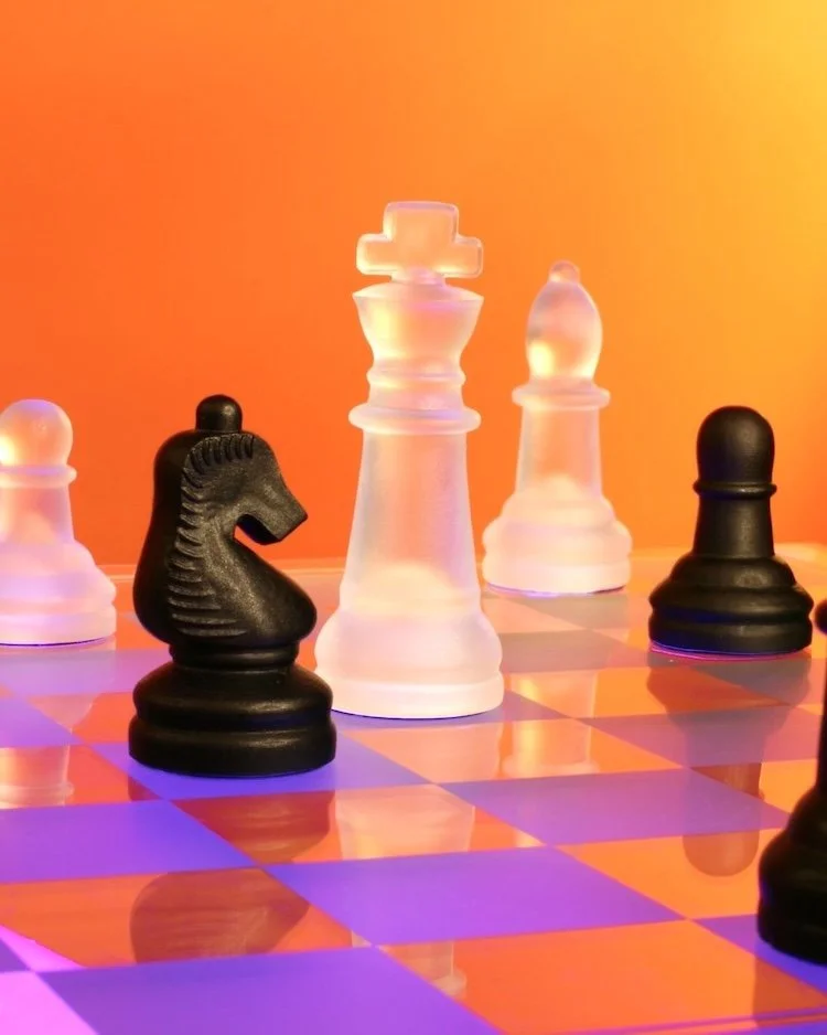 On an orange and purple chess board there are black and white chess pieces to represent being more intentional in your leadership as a result of being in the Not Winging It Leadership Club.