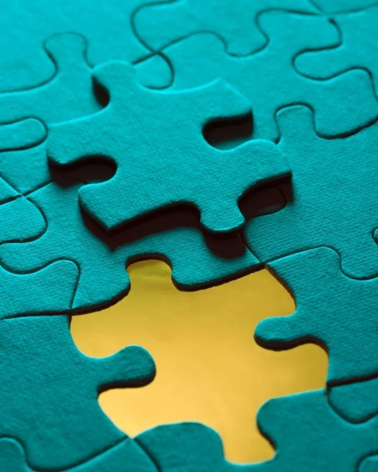 Turquoise coloured jigsaw piece, out of place, lying on top of other pieces of the same colour. you can see a yellow background underneath. To represent the isolation that can be felt as a leader. The Not Winging It Leadeship Club.